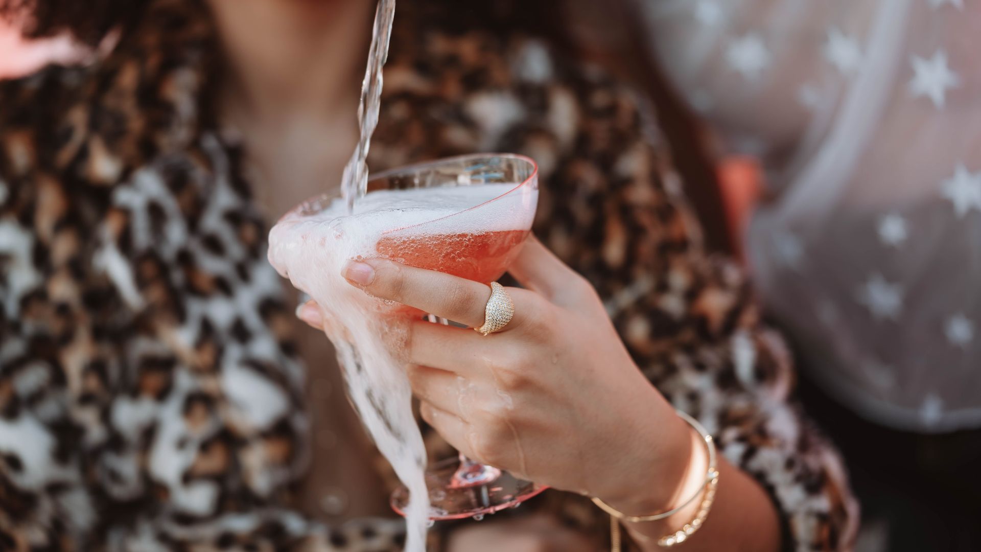 Close-up of a woman in leopard print pouring a luxury cocktail with foam overflowing.
