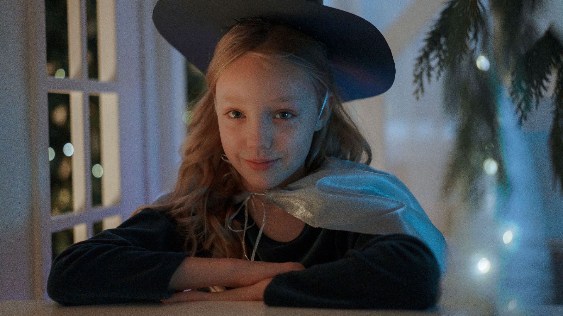 Enchanting young girl dressed as a wizard, sitting near window with magical ambiance.