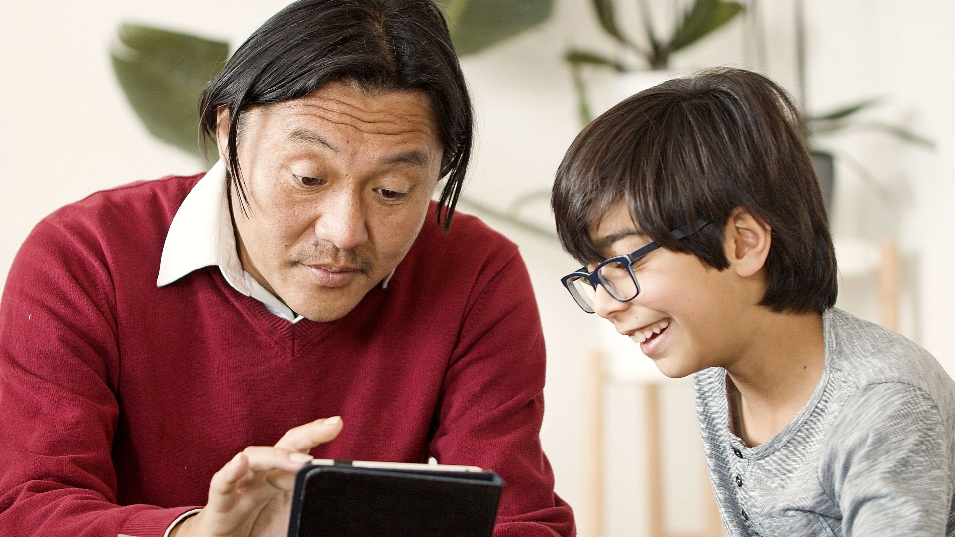 Asian father and child using tablet together in cozy indoor setting.