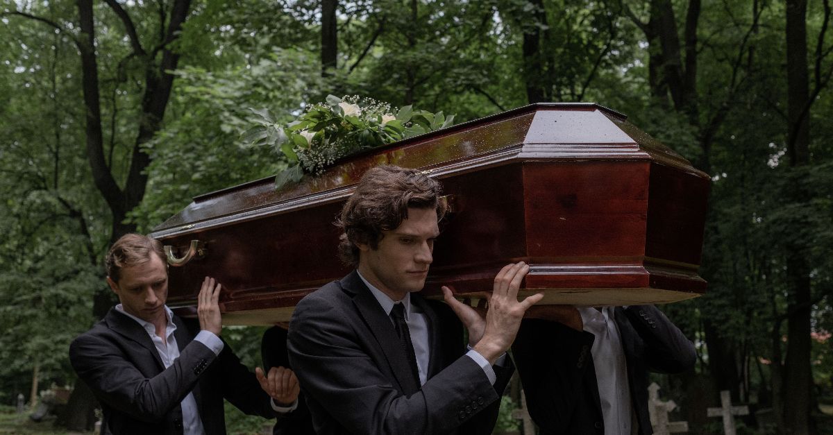 Men solemnly carrying a coffin through a cemetery, symbolizing loss and mourning.