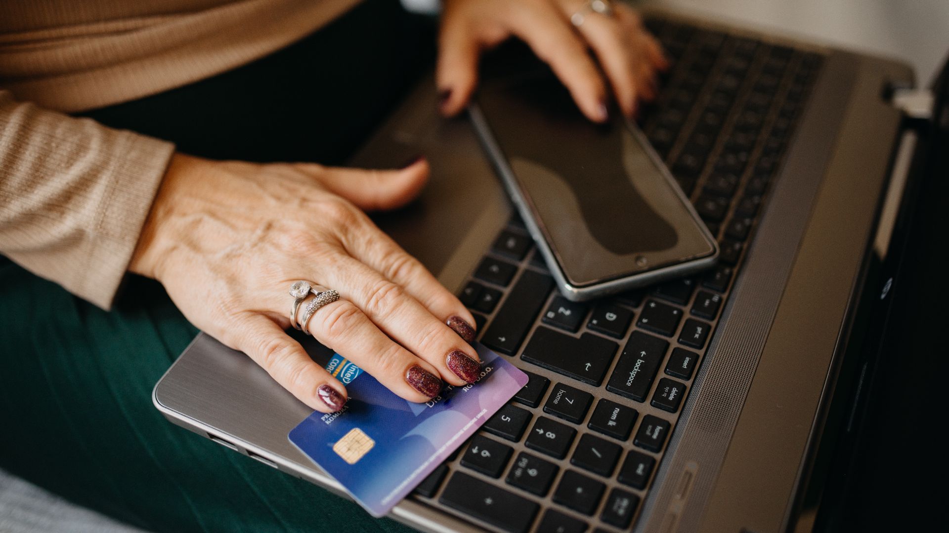 Middle-aged woman holding a credit card and smartphone on the laptop