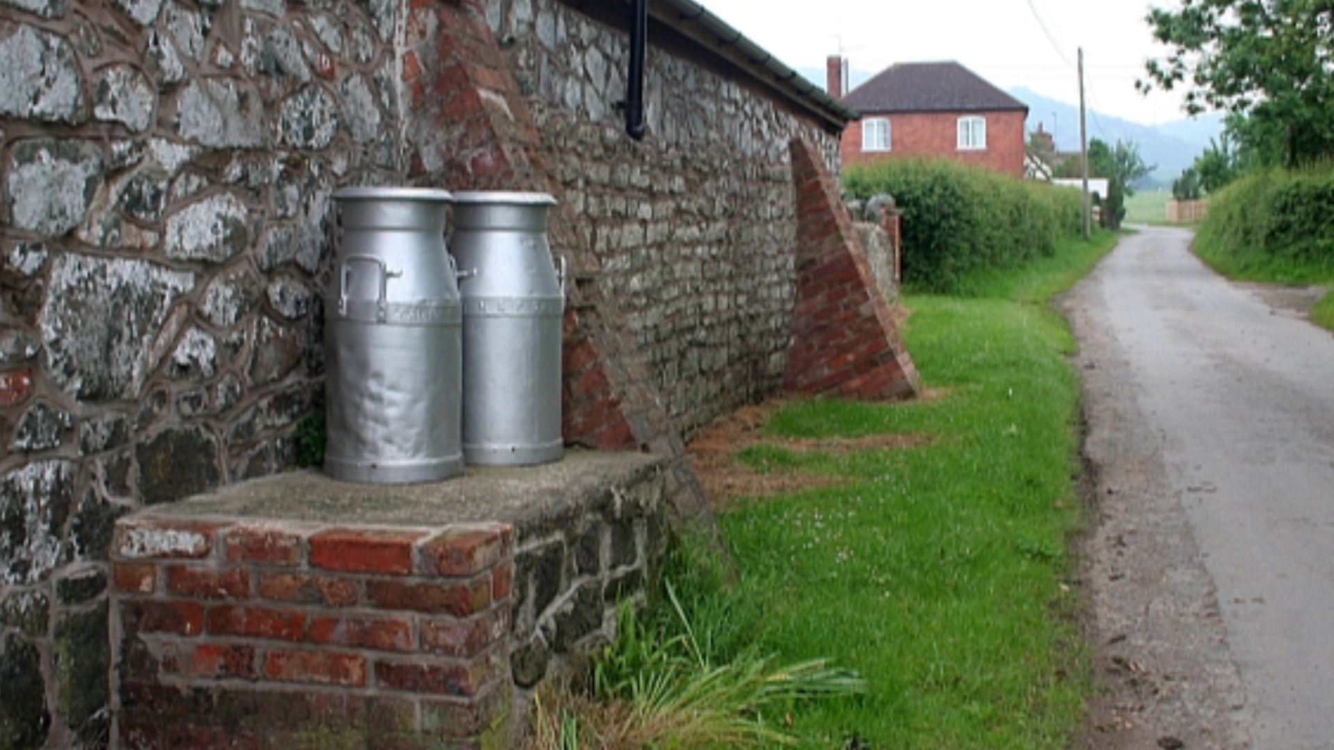 Milk churns on stand, Hollybed Street. Used in older times for the collection of milk from small farms. Placed on a stand for the milk lorry to arrive. Now purely ornamental. One of these belonged to