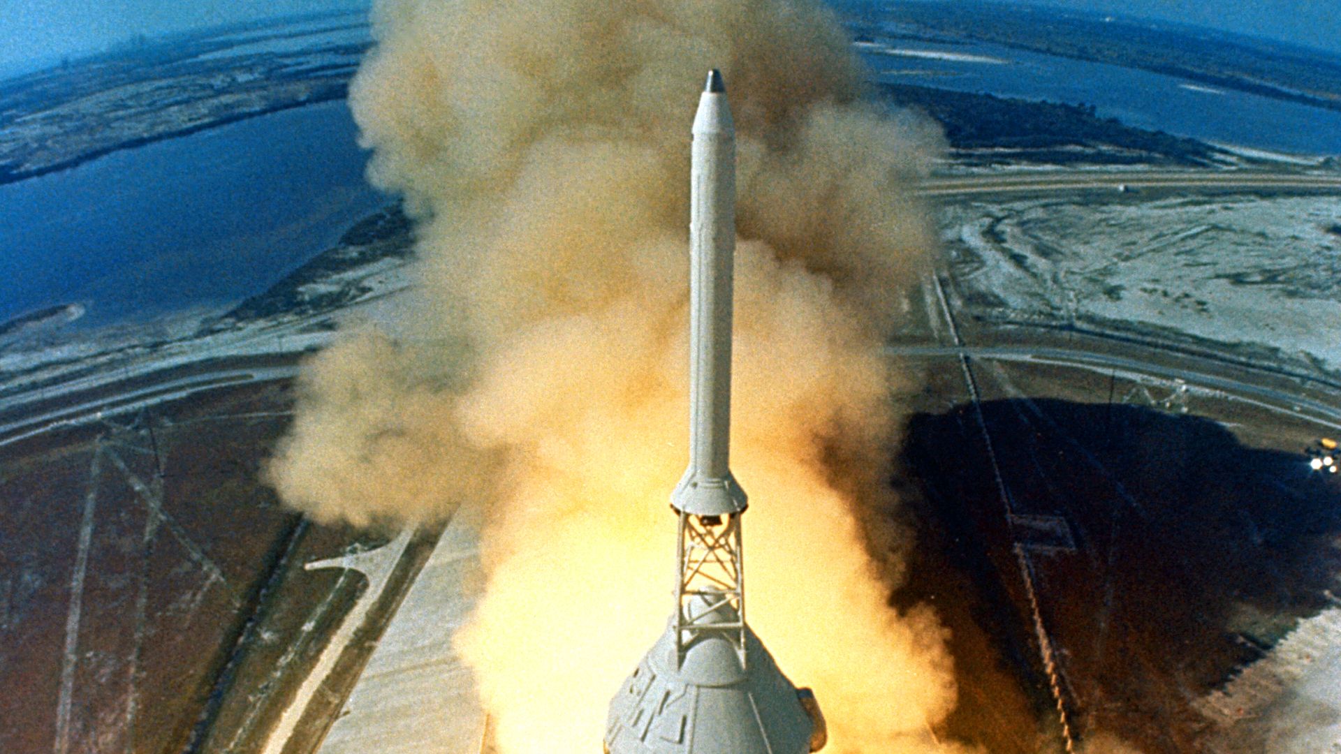 At 9:32 a.m. EDT, the swing arms move away and a plume of flame signals the liftoff of the Apollo 11 Saturn V space vehicle and astronauts Neil A. Armstrong, Michael Collins and Edwin E. Aldrin, Jr. from Kennedy Space Center Launch Complex 39A.