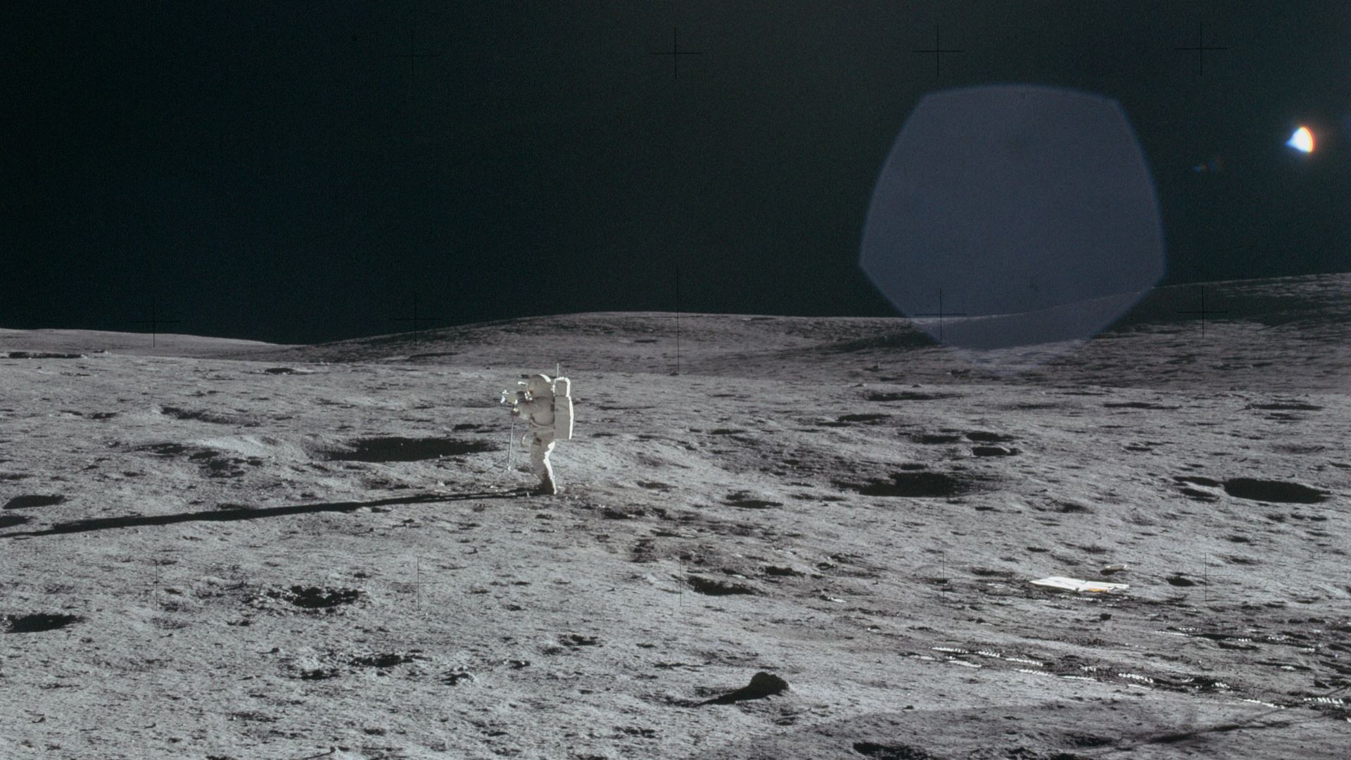 Frame from Al's 12 o'clock pan showing Ed doing a TV pan and, in the distance, considerable detail of the Cone Crater ridge. We can see Ed's footprints leading out to the TV site. As is usual for soil disturbances near the LM, the soil along Ed's track is