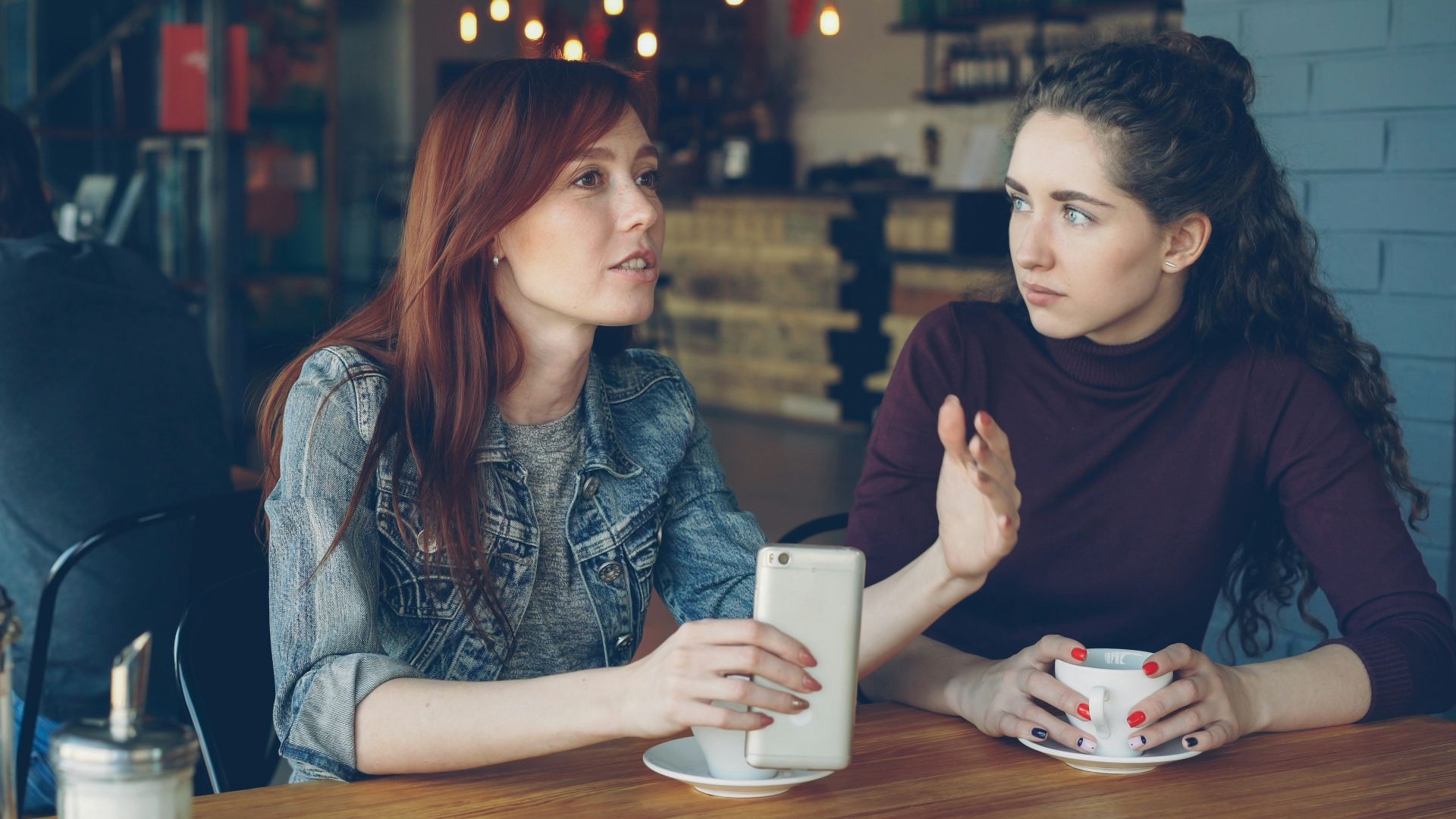 Two women converse at a cafe.