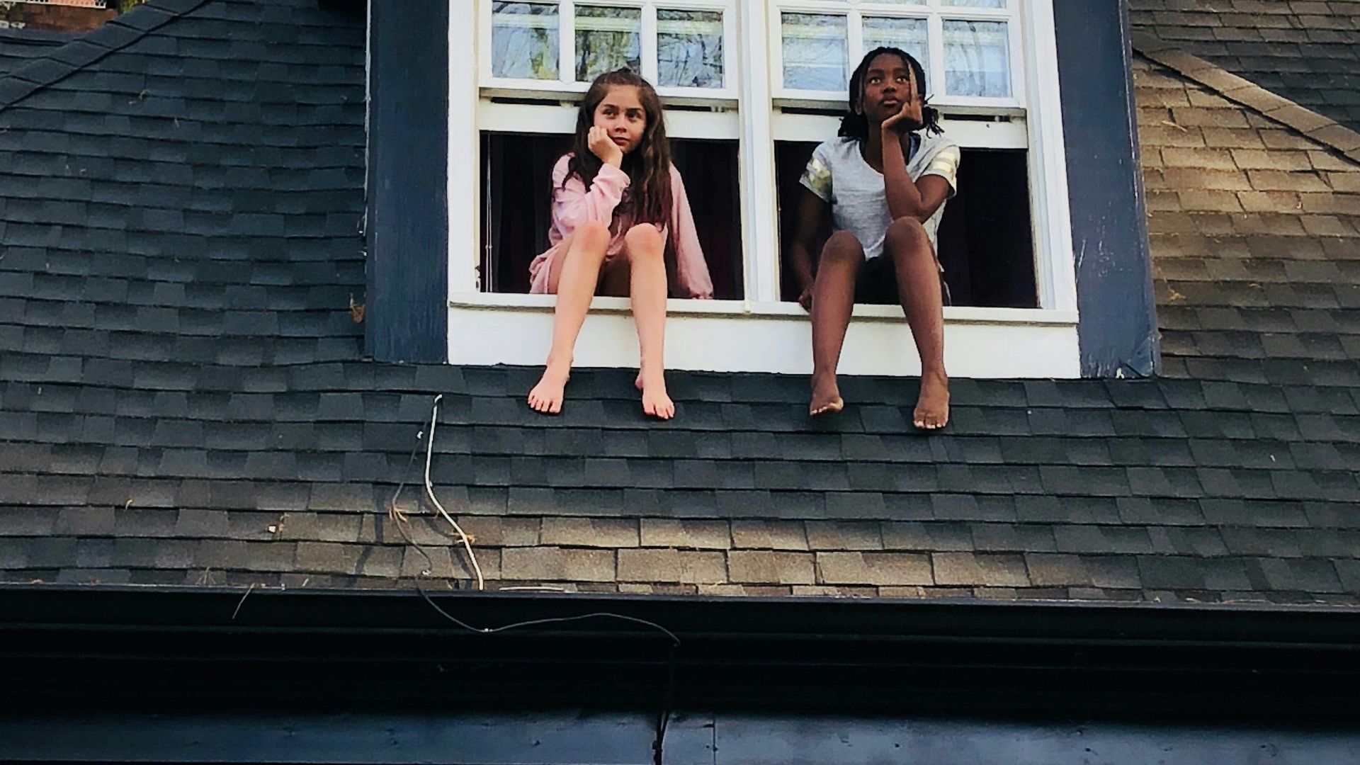 two girls sitting on white 2-panel windows during daytime