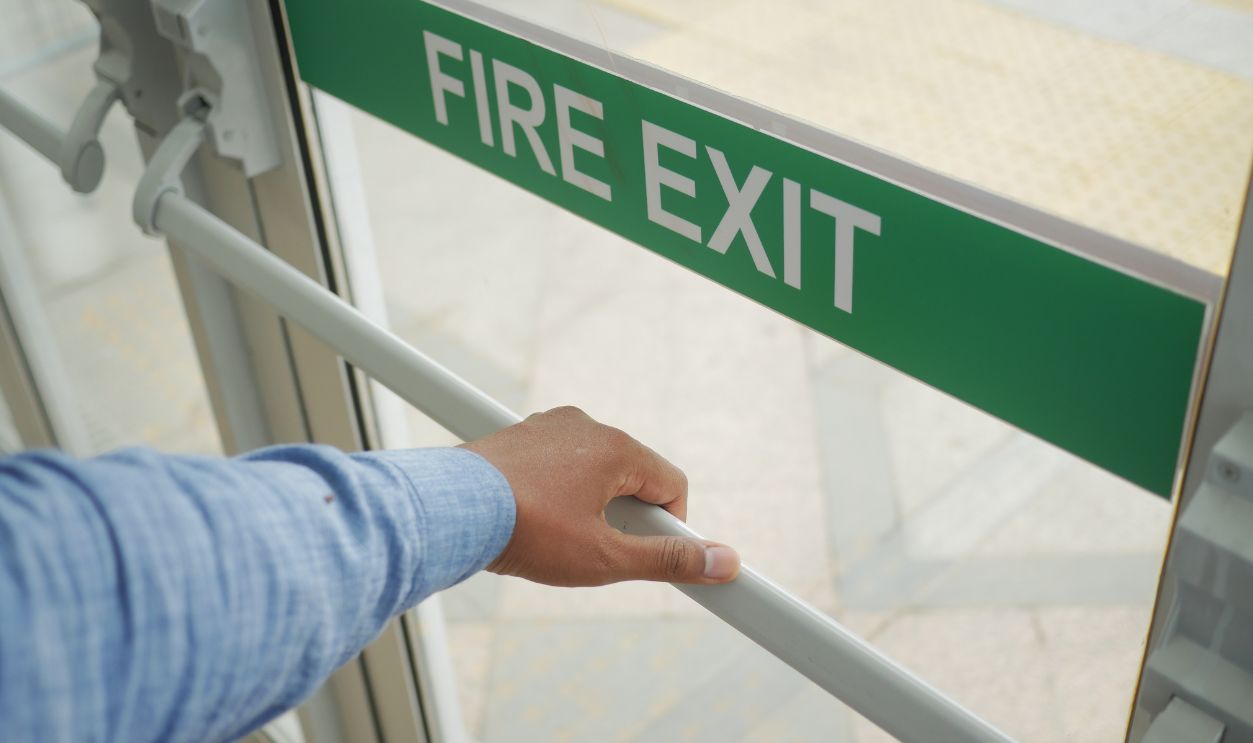 A person is using their hand to open a fire exit door for a vital emergency evacuation