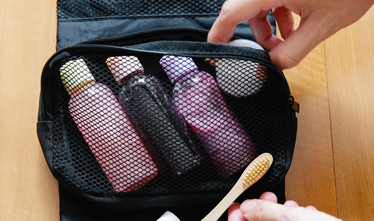 Open toiletry bag with bottles and a bamboo toothbrush on wooden surface