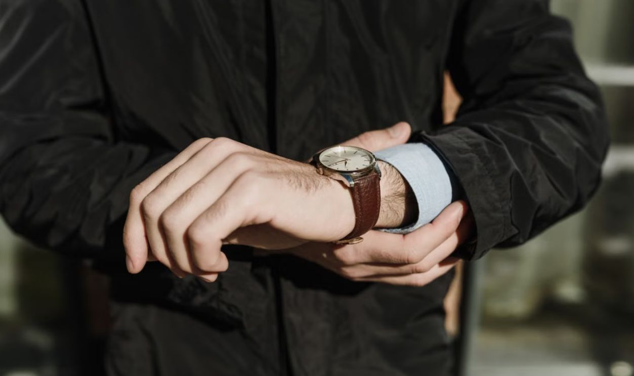 Close-up of a man's hands adjusting a classic leather watch outdoors