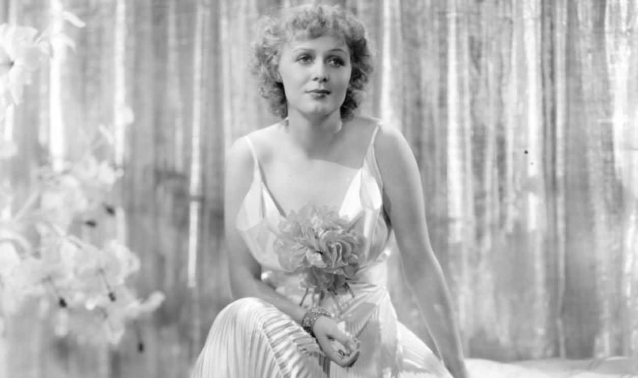 circa 1935: Gloria Stuart, the stage name of Gloria Stuart Finch ( 1909 - ) the American leading lady of the thirties is pictured wearing a glamorous evening dress of white satin with a draped bodice, especially designed for the 20th Century Fox film 'Poor Little Rich Girl' which she is starring in.