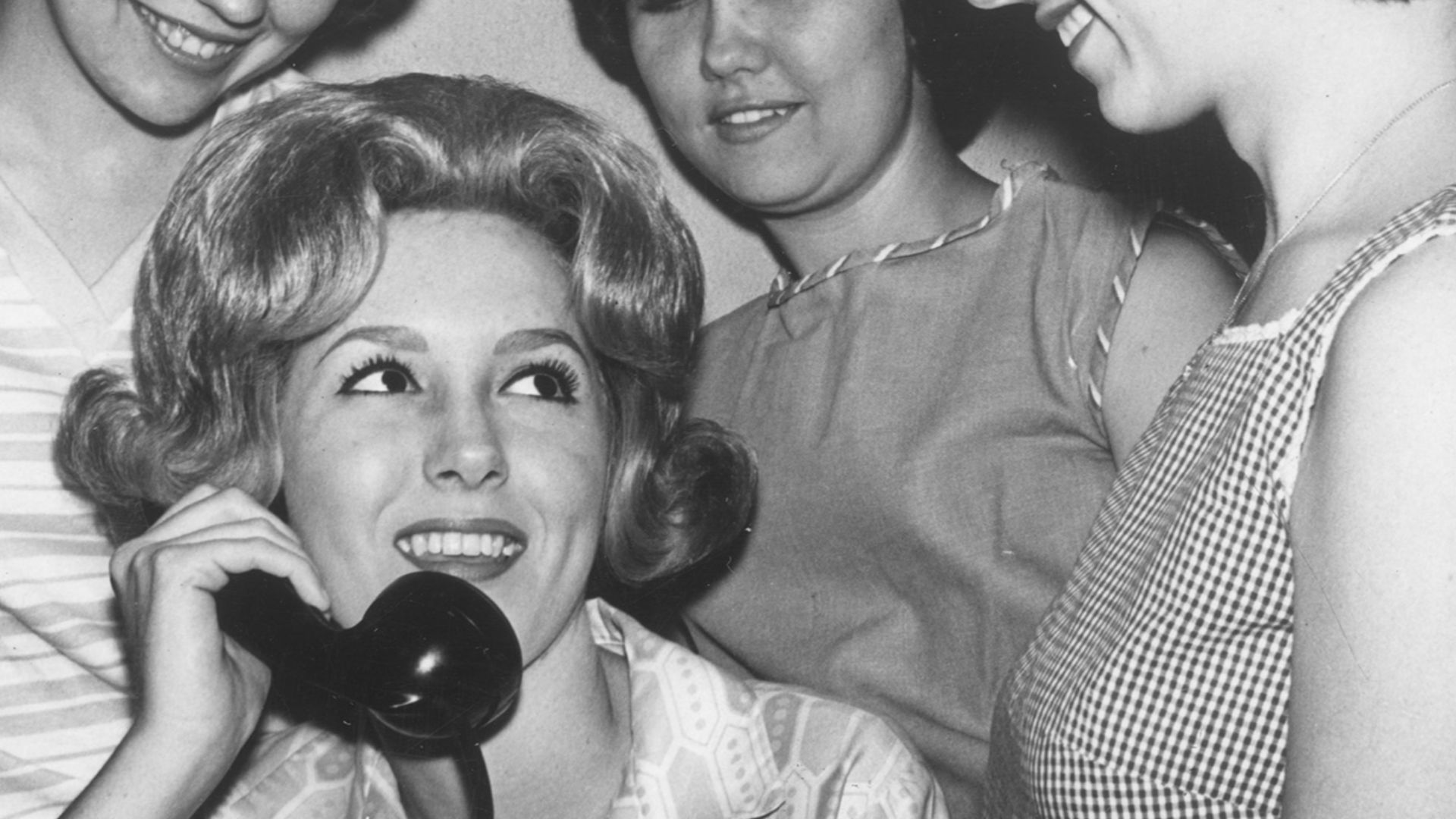 Four female students huddled around telephone, Arlington State College.