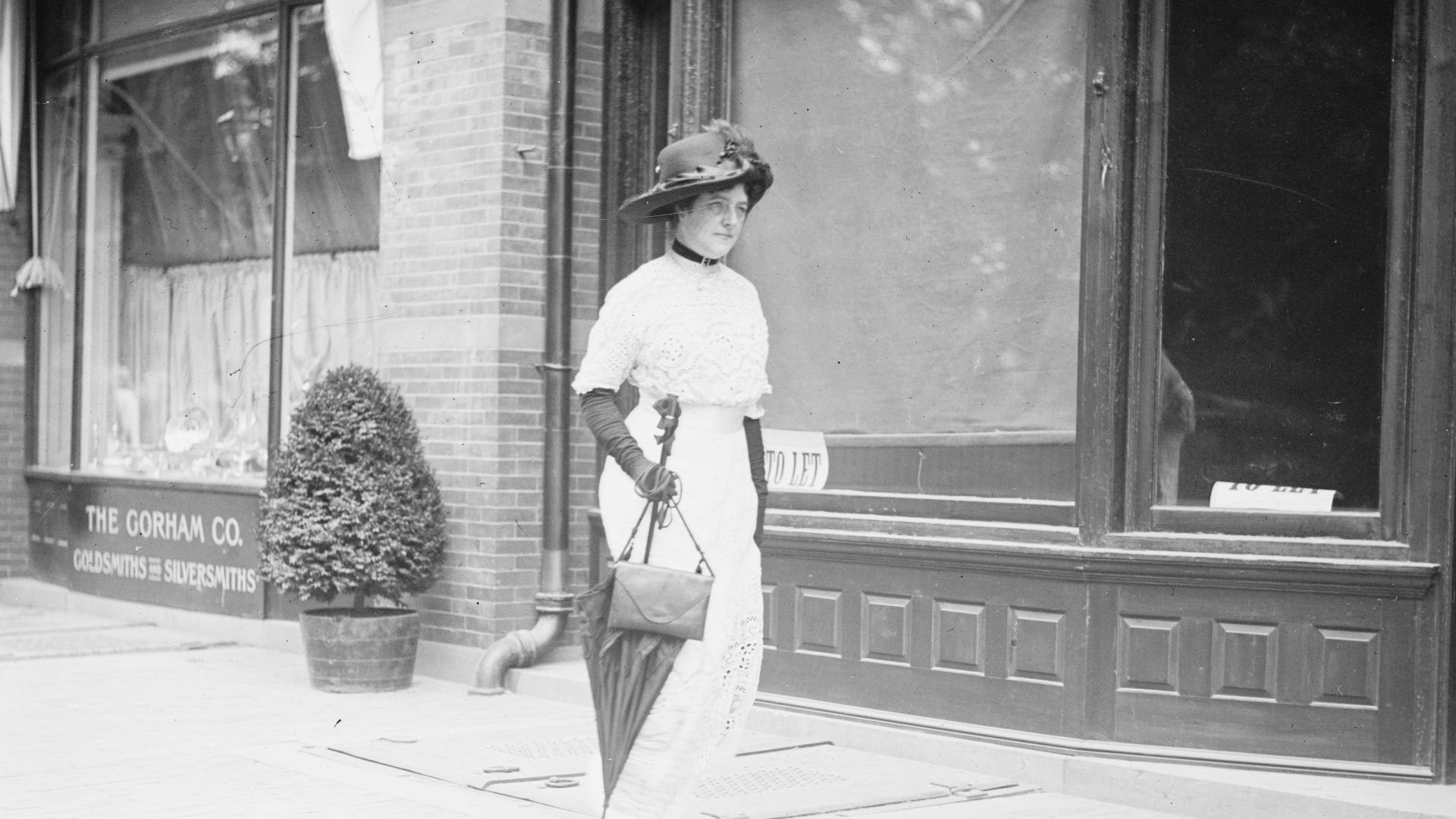 Title: Mrs. Burke Roche walking on sidewalk with parasol
Abstract/medium: 1 negative : glass ; 5 x 7 in. or smaller.