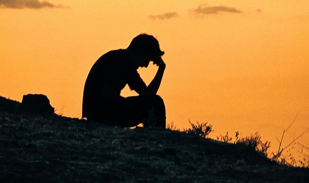 Silhouette of a person sitting on a hill against a vibrant sunset sky, evoking contemplation