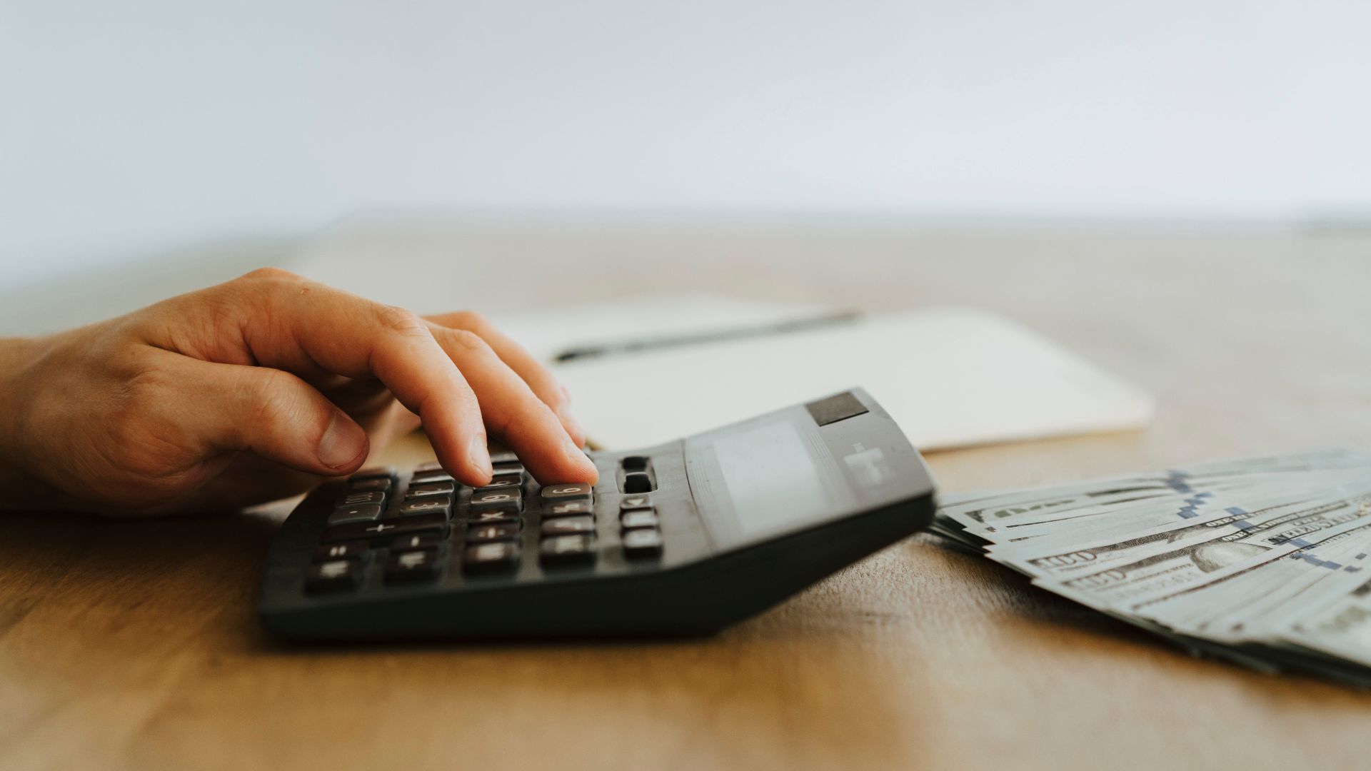 A hand calculating finances with a calculator next to stacks of US dollar bills.