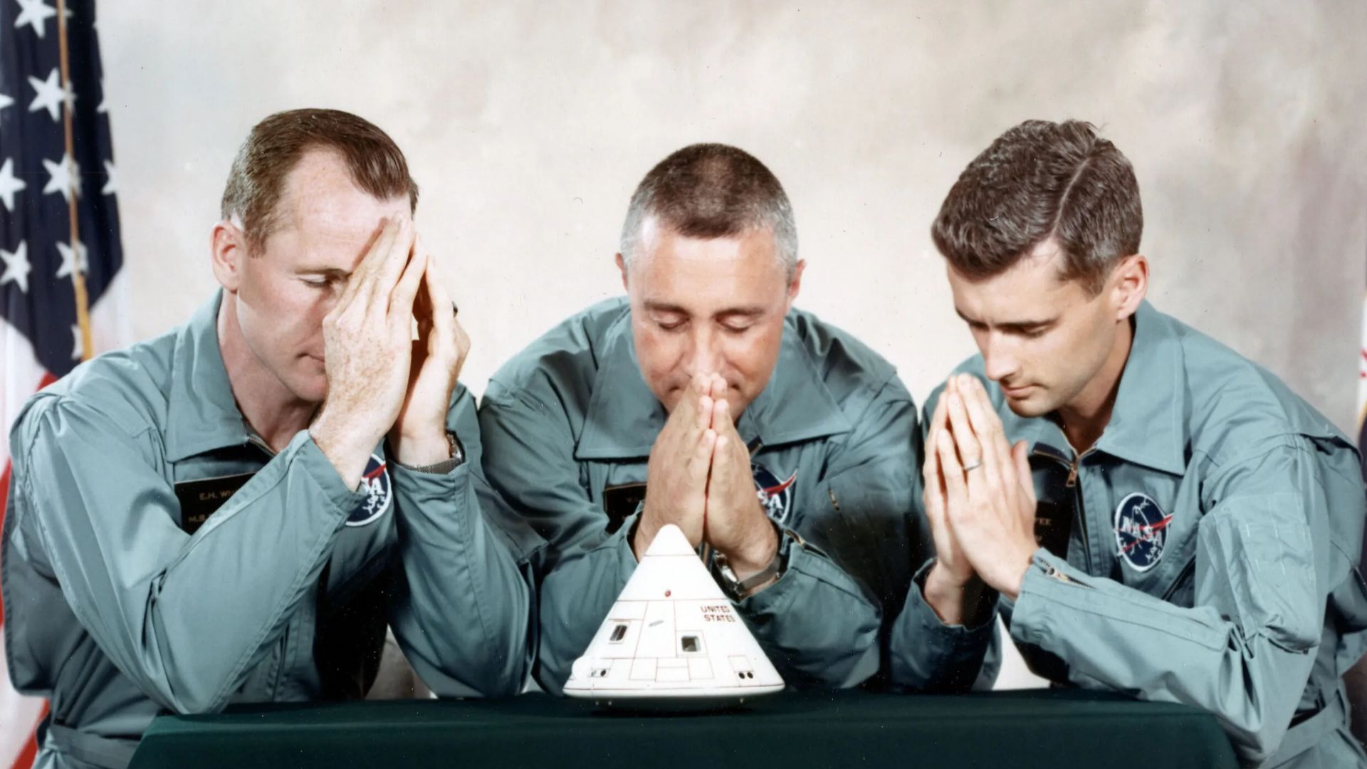 The astronaut crew of Apollo 1 praying, with a model of the Command Module spacecraft on the table in front of them. From left to right: Ed White, Virgil Ivan