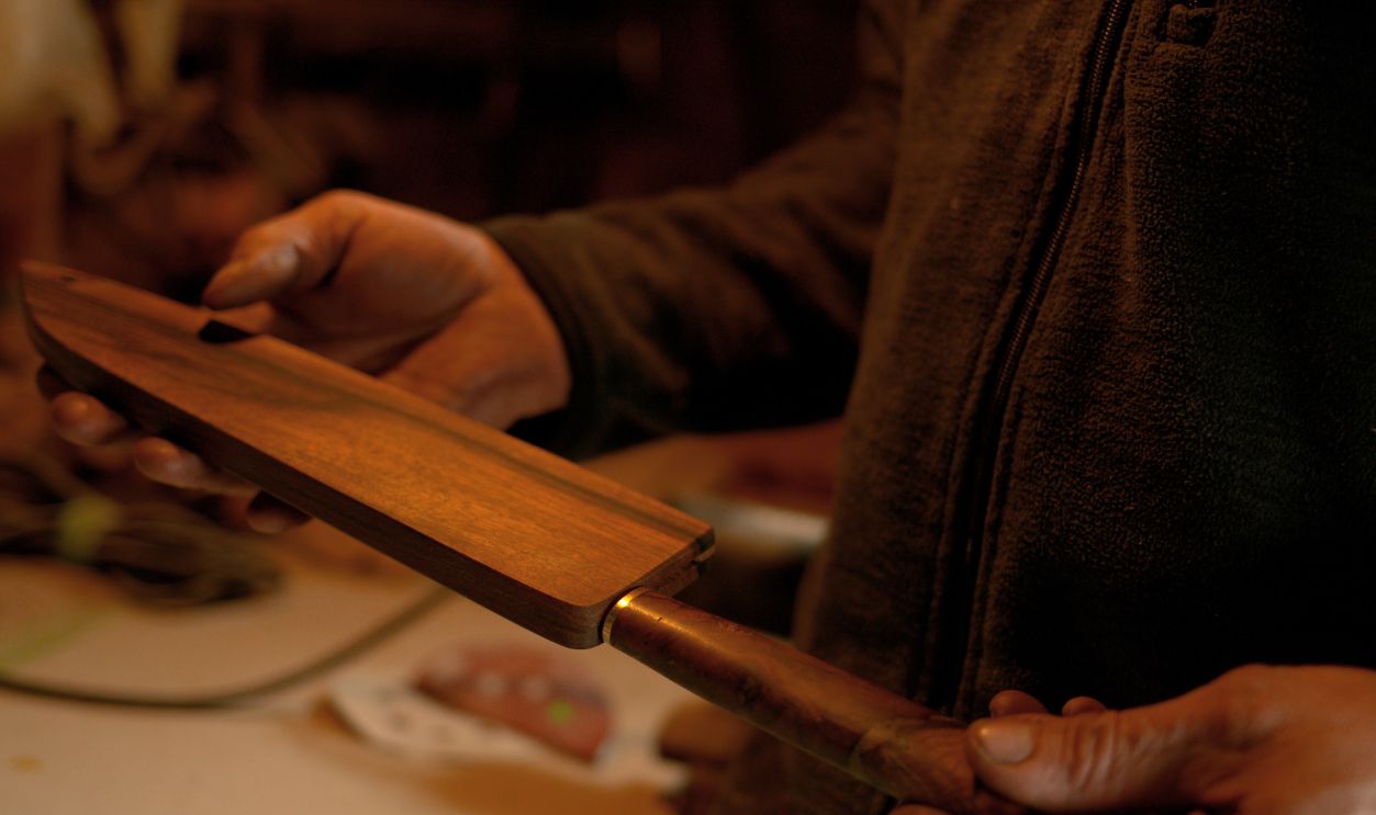 CLOSE UP, DOF: Bladesmith proudly looks at a finished knife inside a wooden sheath. Unrecognizable man holding a traditionally handcrafted knife with a wooden handle inside a beautiful oak cover.