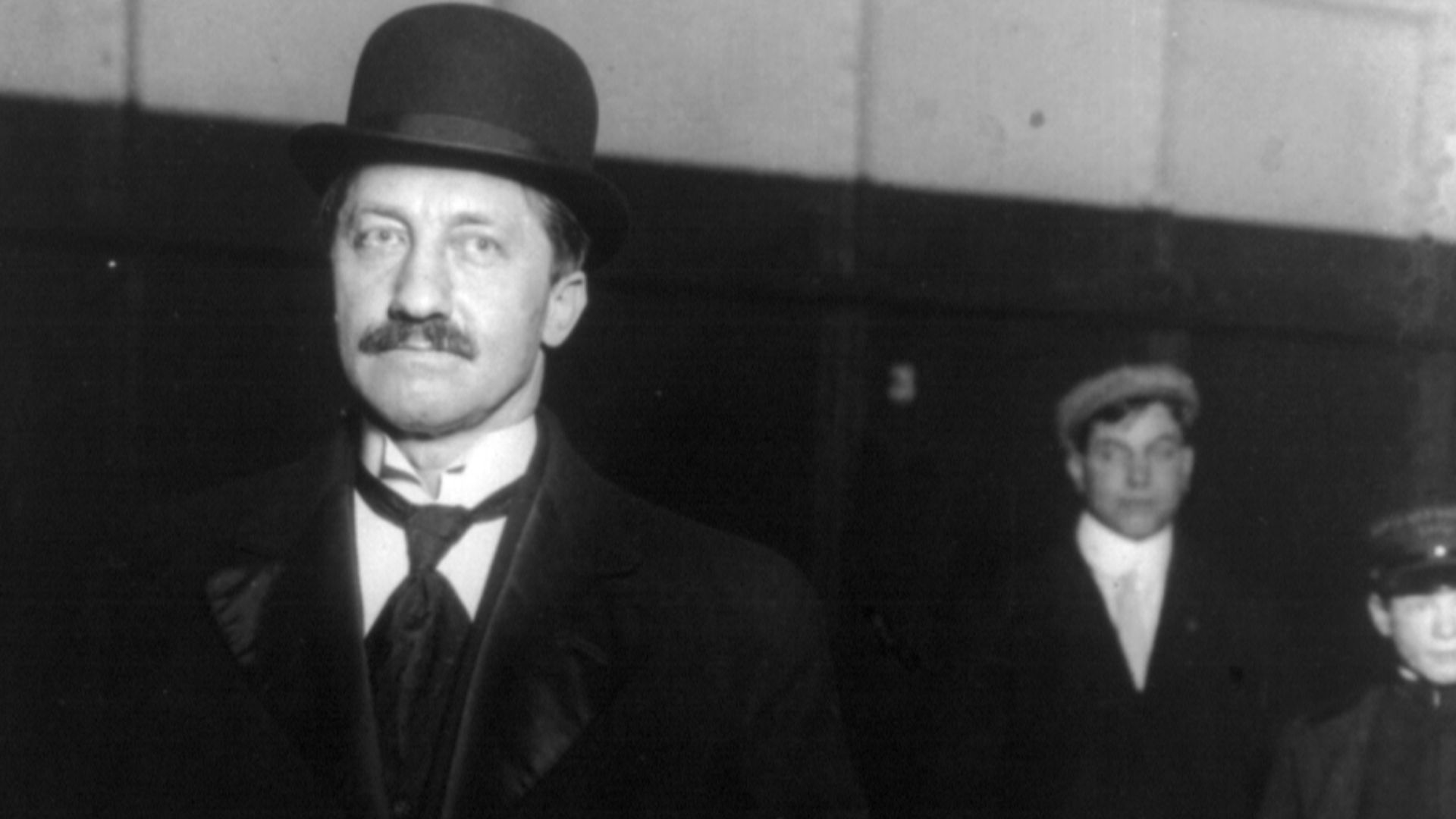 Frederick Cook, standing, facing left, holding umbrella and gloves, with two unidentified men in background.