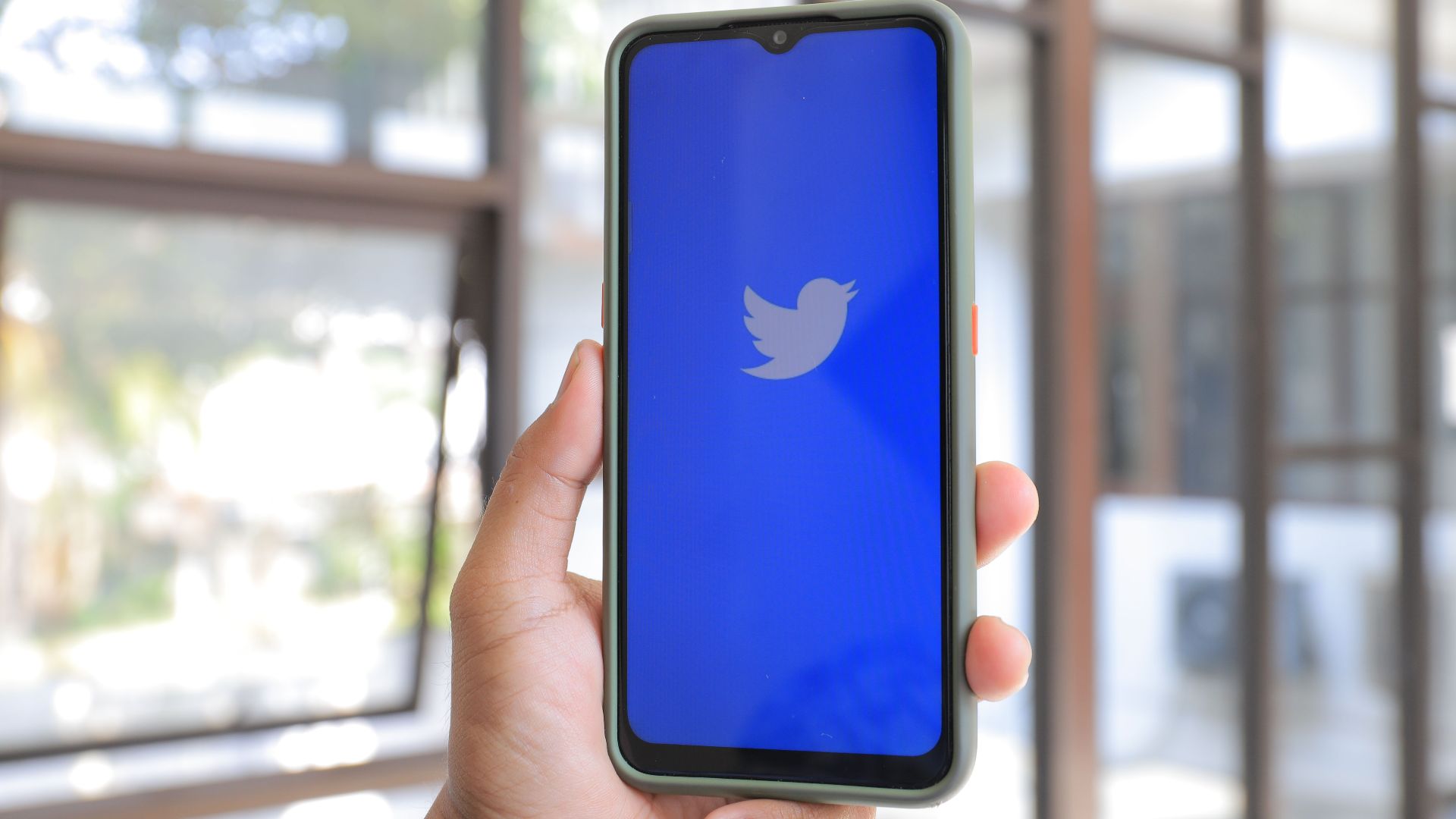 Hand holding a smartphone displaying the Twitter logo, indoors with natural light.