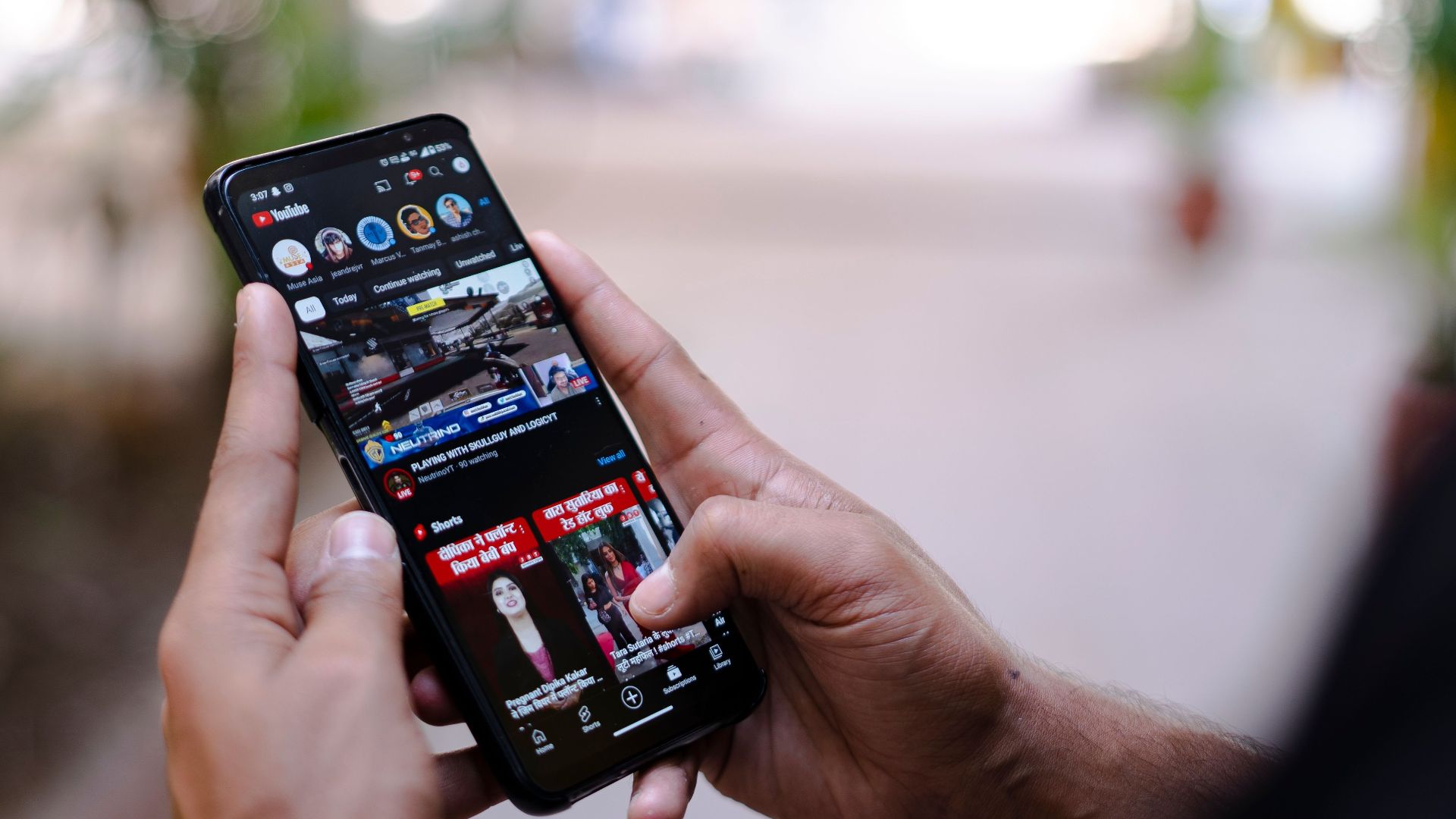 Close-up of hands using a smartphone to watch YouTube outdoors, showcasing digital connectivity.