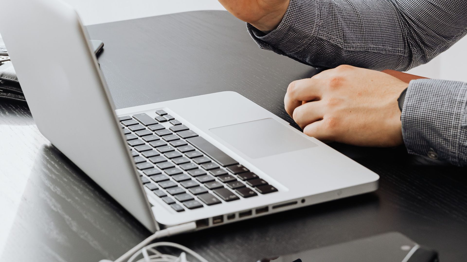 Close-up of a person using a laptop in a modern office setting with electronic devices on the table.