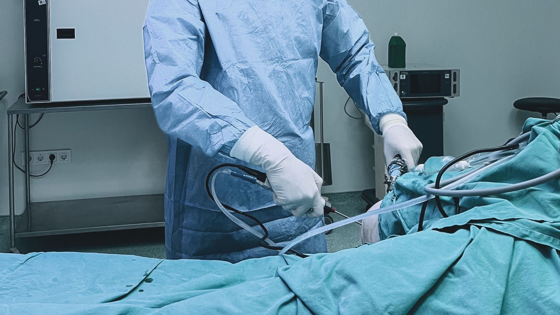 A surgeon in a blue gown performing an endoscopic procedure in an equipped operating room.