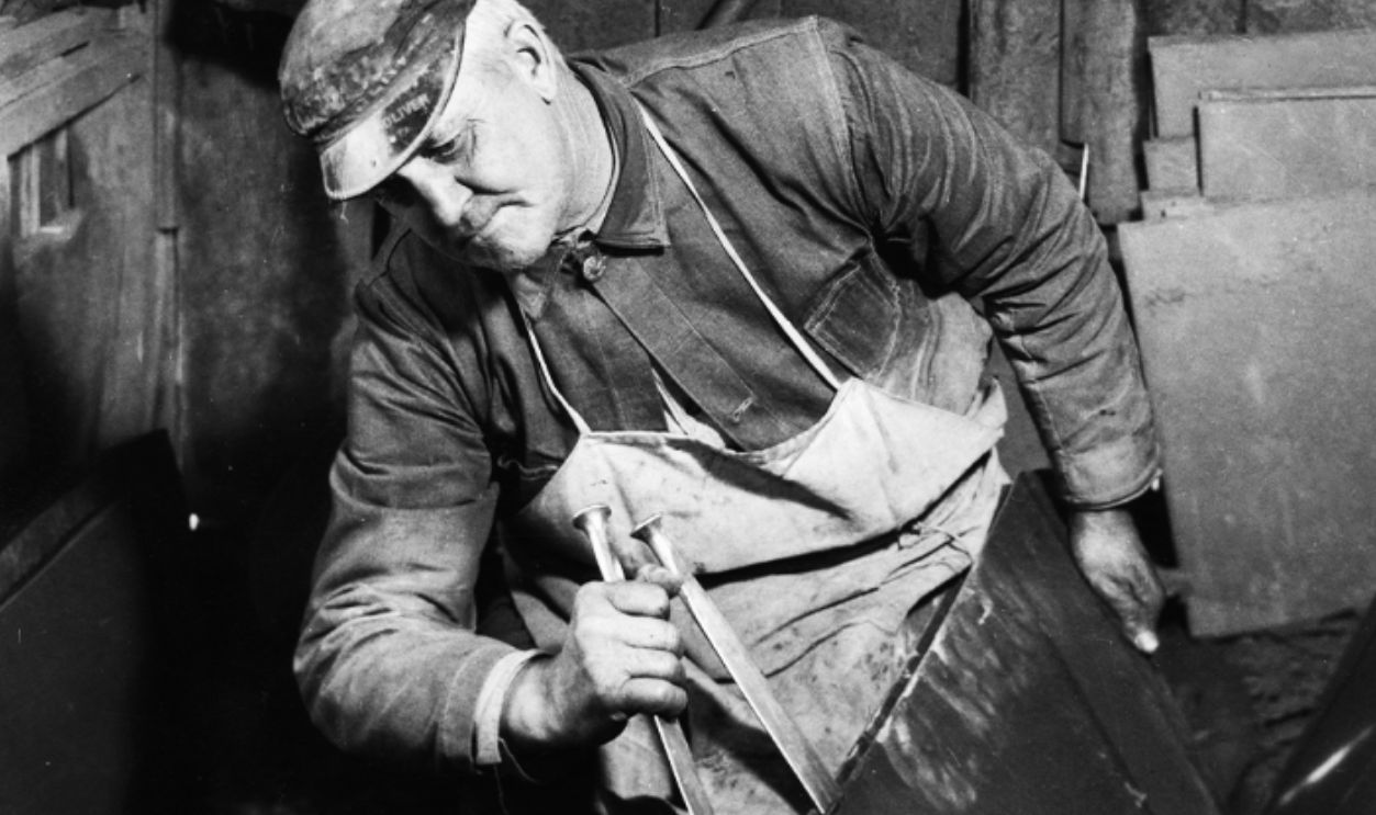 A slate worker using chisels to split a sheet of slate for the production of roof shingles, at a slate quarry in Bangor, Pennsylvania, circa 1935. The State of Pennsylvania supplies fifty per cent of the slate used in the United States.
