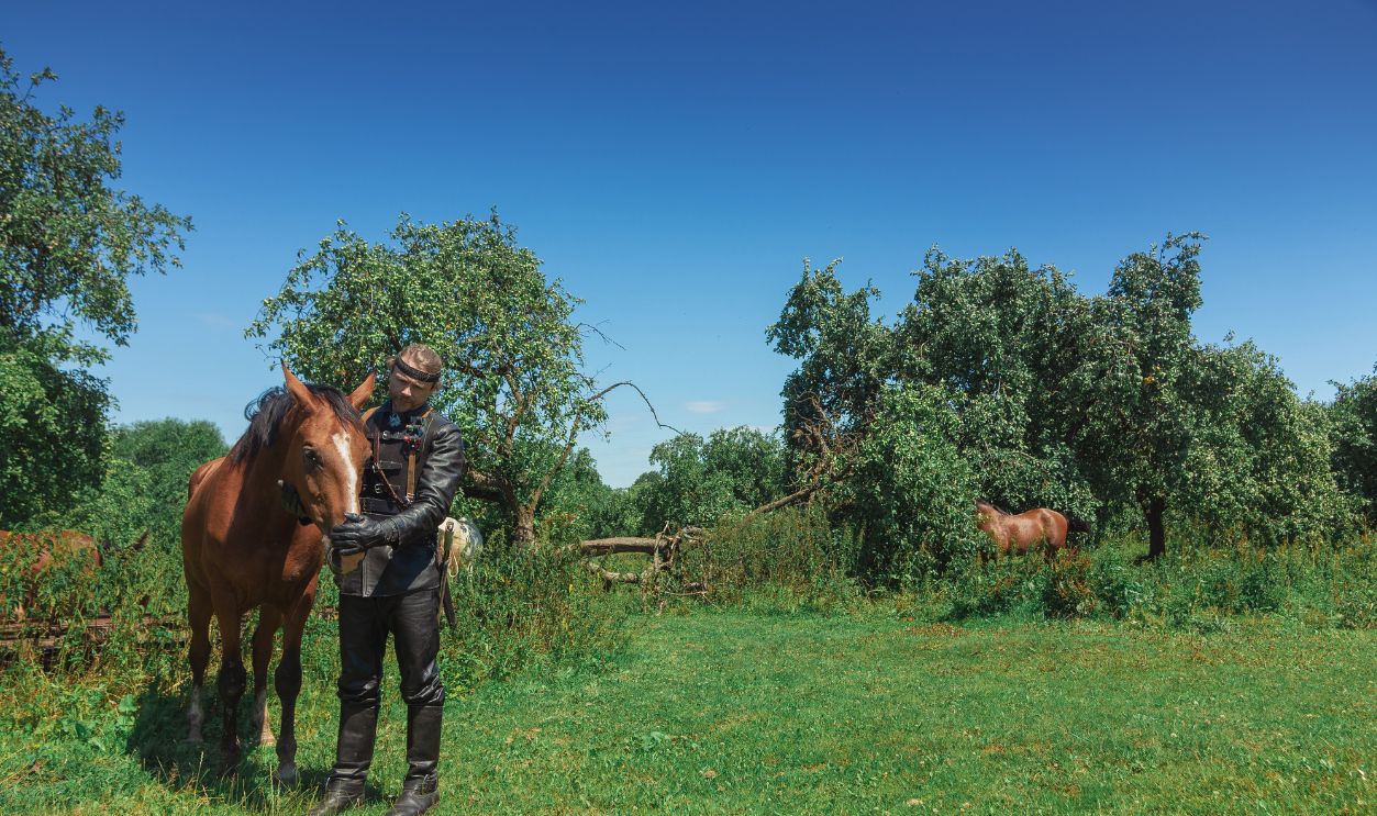 A man in an ancient leather costume knight from fantasy games with horses in the woods