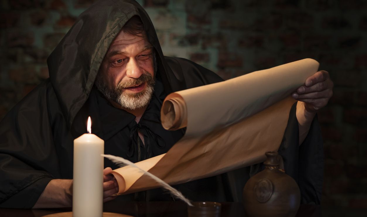 Emotional portrait of an elderly monk, by candlelight reading a message on parchment.