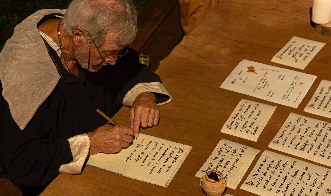 MONZAMBANO, ITALY - SEPTEMBER 20, 2025: An overhead view of a reenactor portraying a medieval scribe, writing calligraphy at his desk during a historical festival.