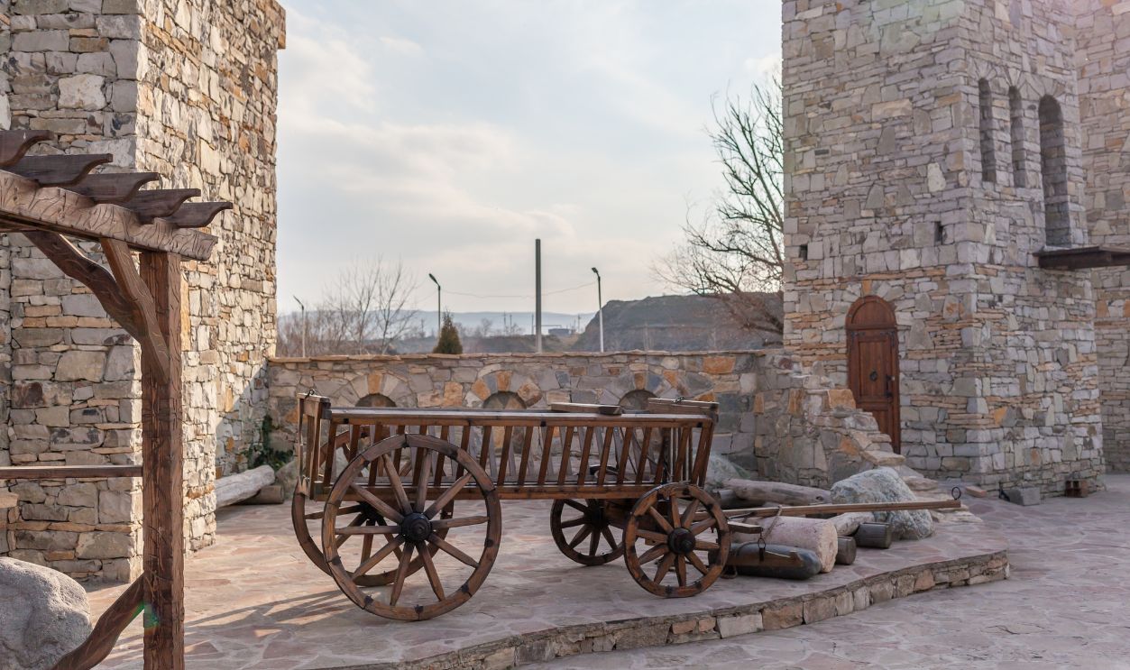 Close-up of an old wooden cart made from logs, used to transport goods, crops or savagery, next to a high stone wall and a stone fence on a sunny summer day in Dagestan.