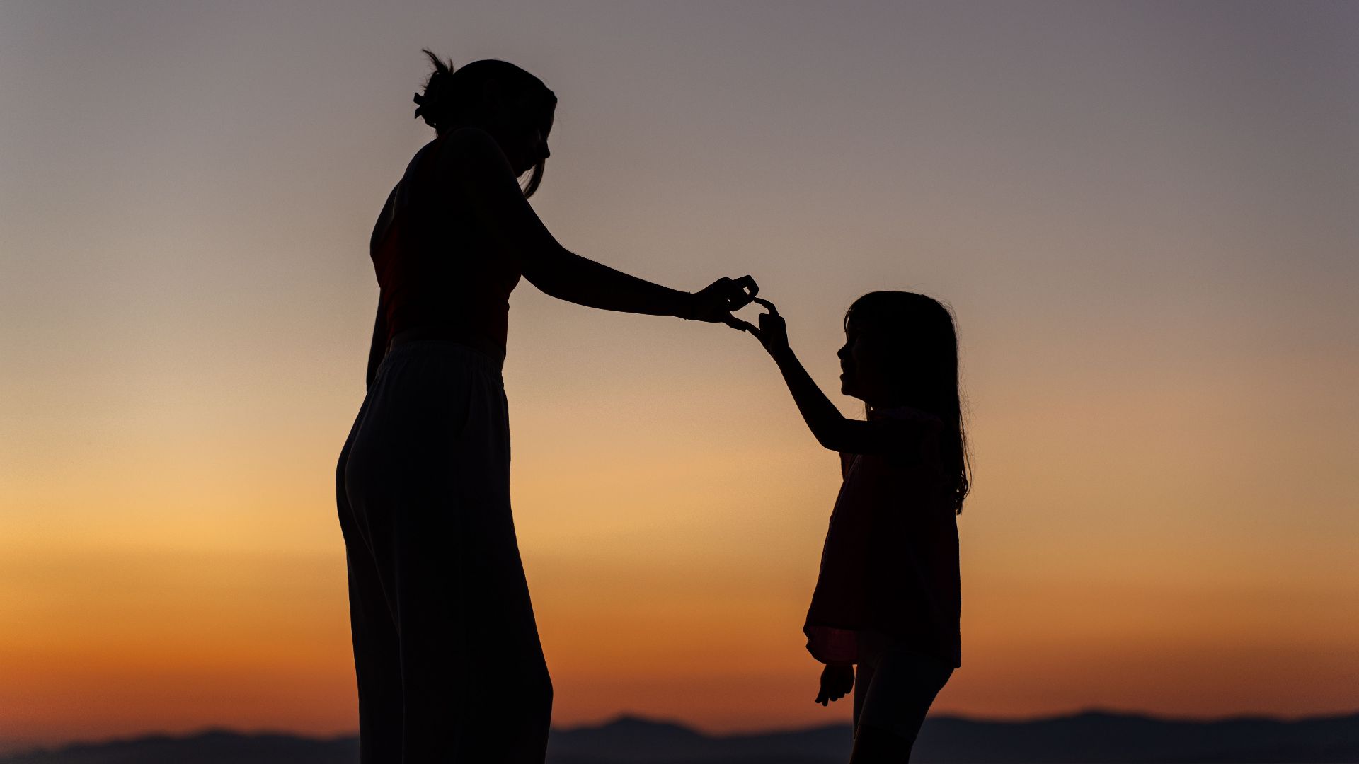 Silhouette of woman and child forming a heart with hands at sunset in Supetar, Croatia.