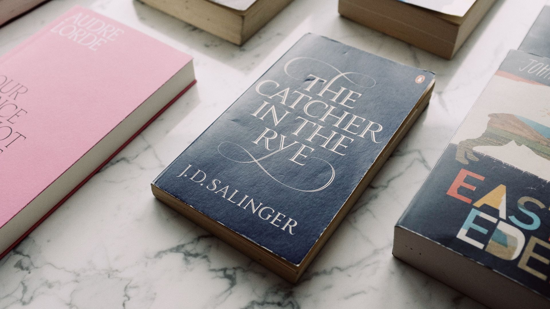 A collection of classic novels displayed on a marble surface, showcasing titles like 'The Catcher in the Rye.'
