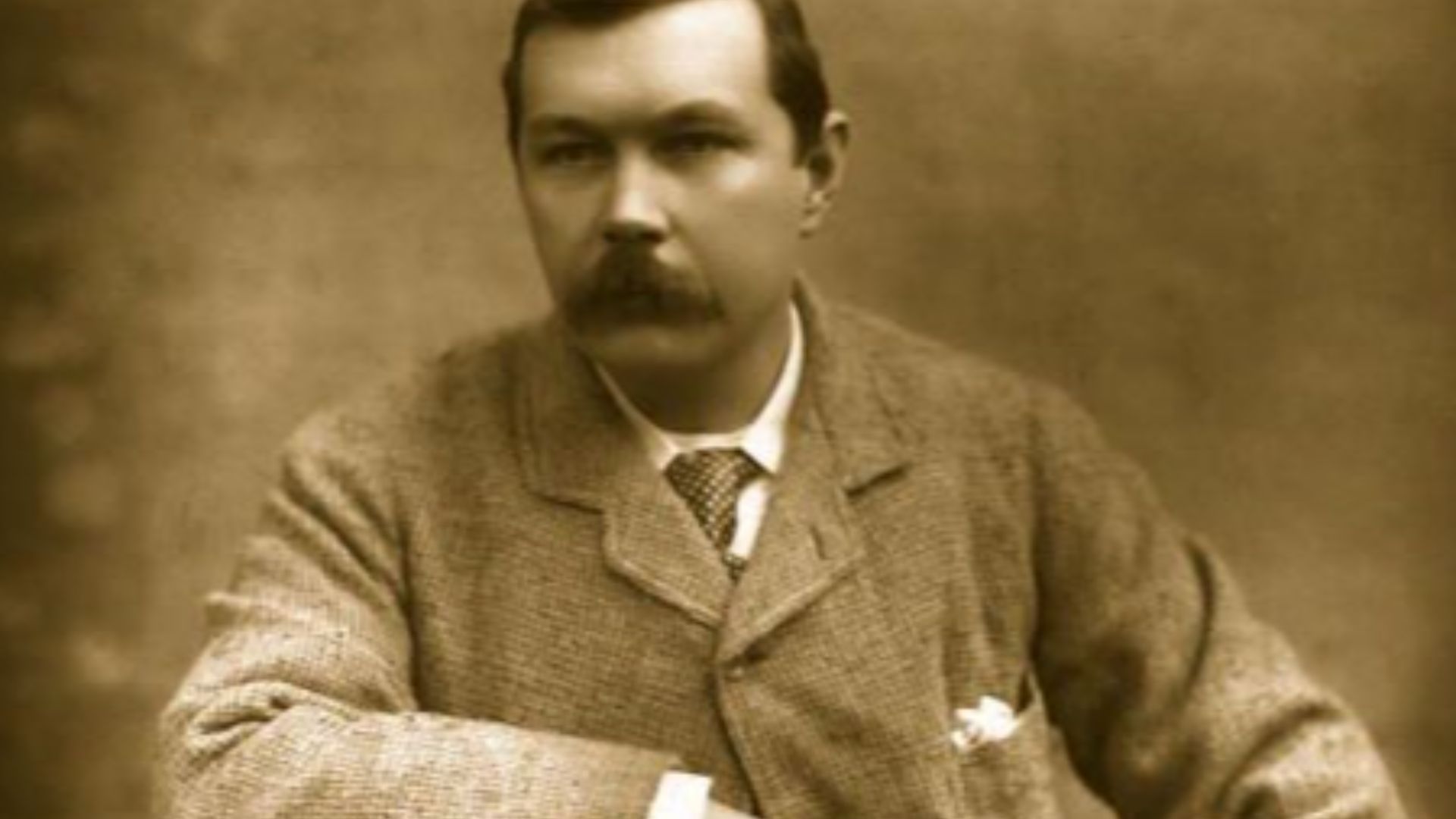 Photograph of Arthur Conan Doyle, seated sideways on chair. Published in