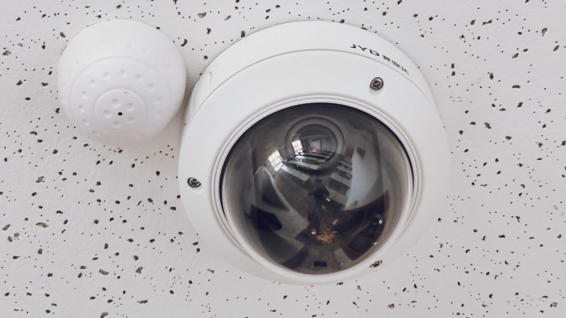 Close-up of a round dome surveillance camera installed on a speckled ceiling for security monitoring.