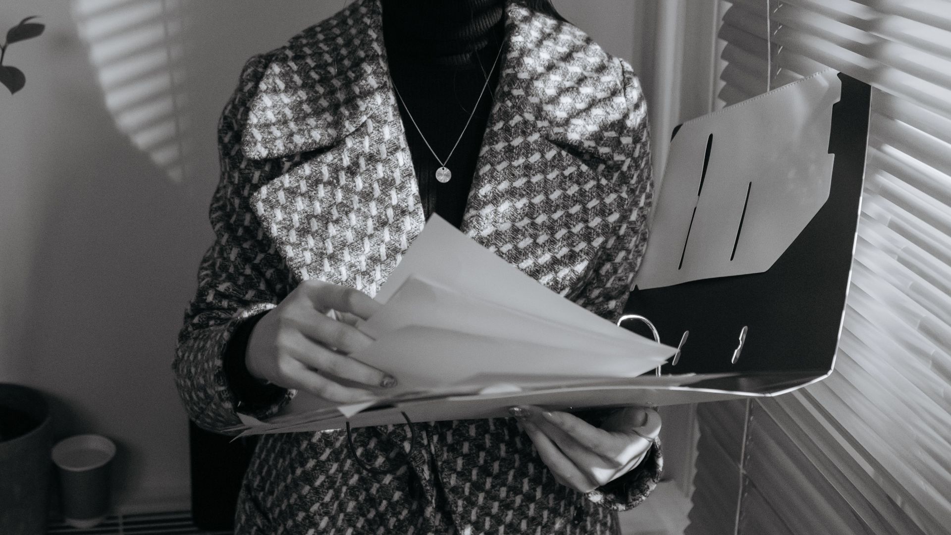 Business woman in black and white, reviewing documents with blinds creating shadows.