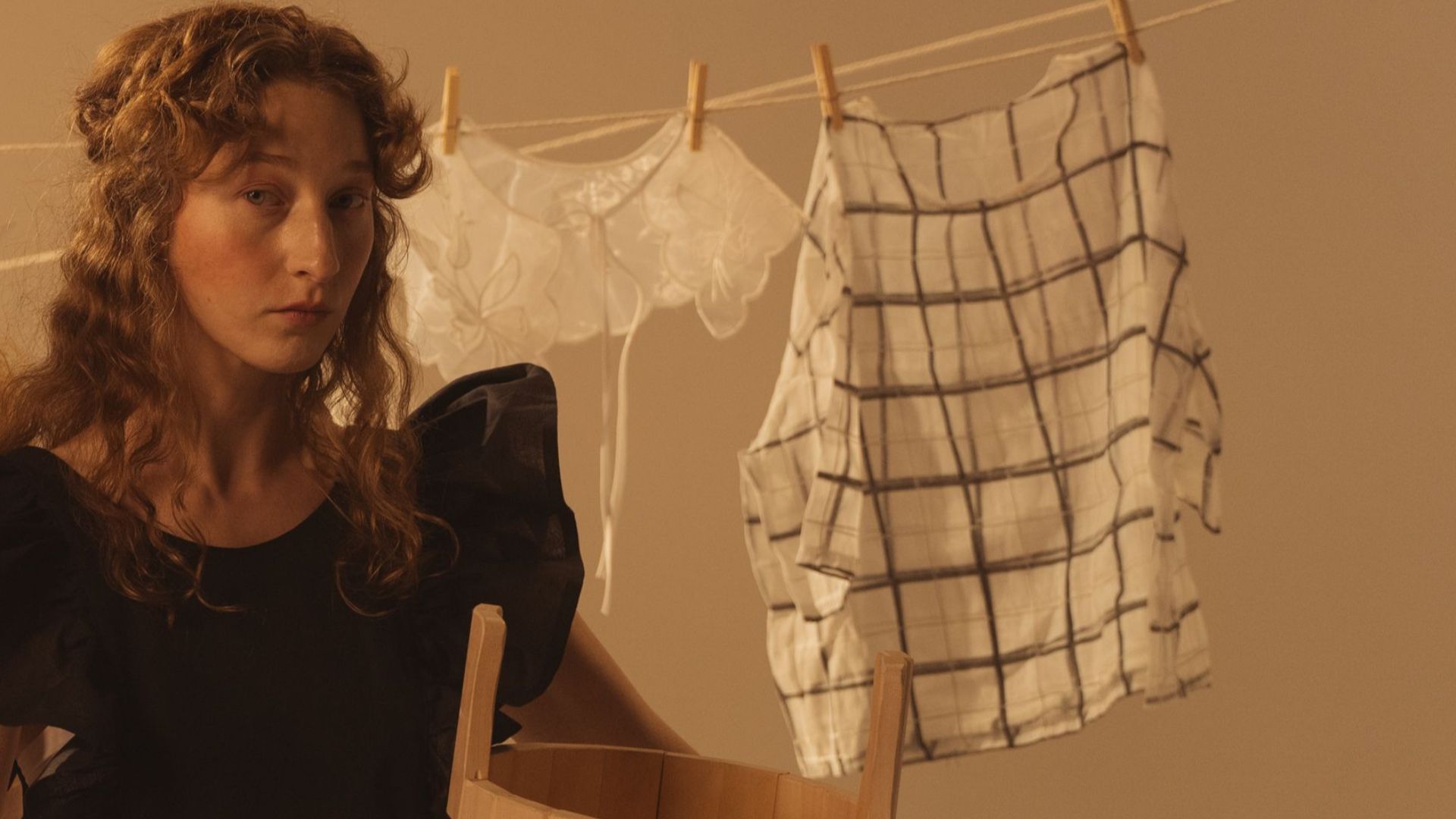 Two women in vintage dresses holding metal basins, with clothes hanging on a line in a rustic setting.