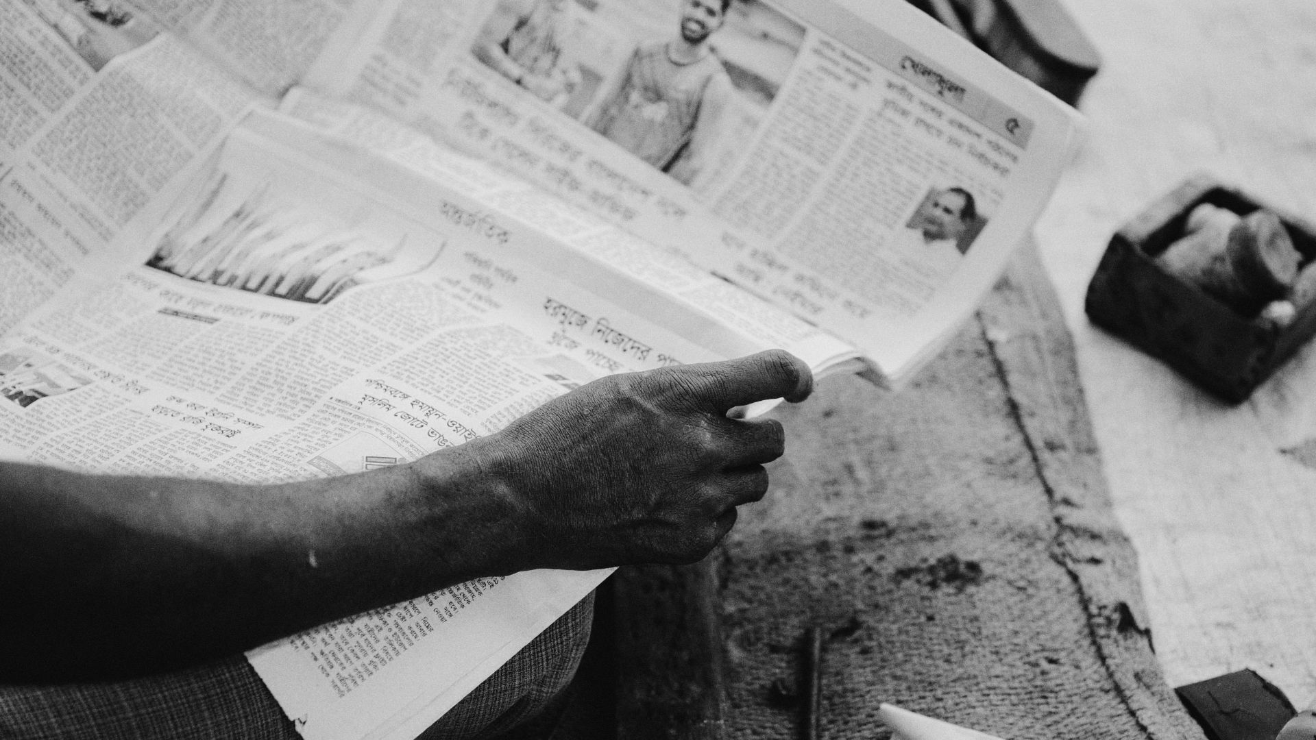 A person reads a newspaper on a street in Kurigram, Bangladesh, capturing daily life in a monochrome style.
