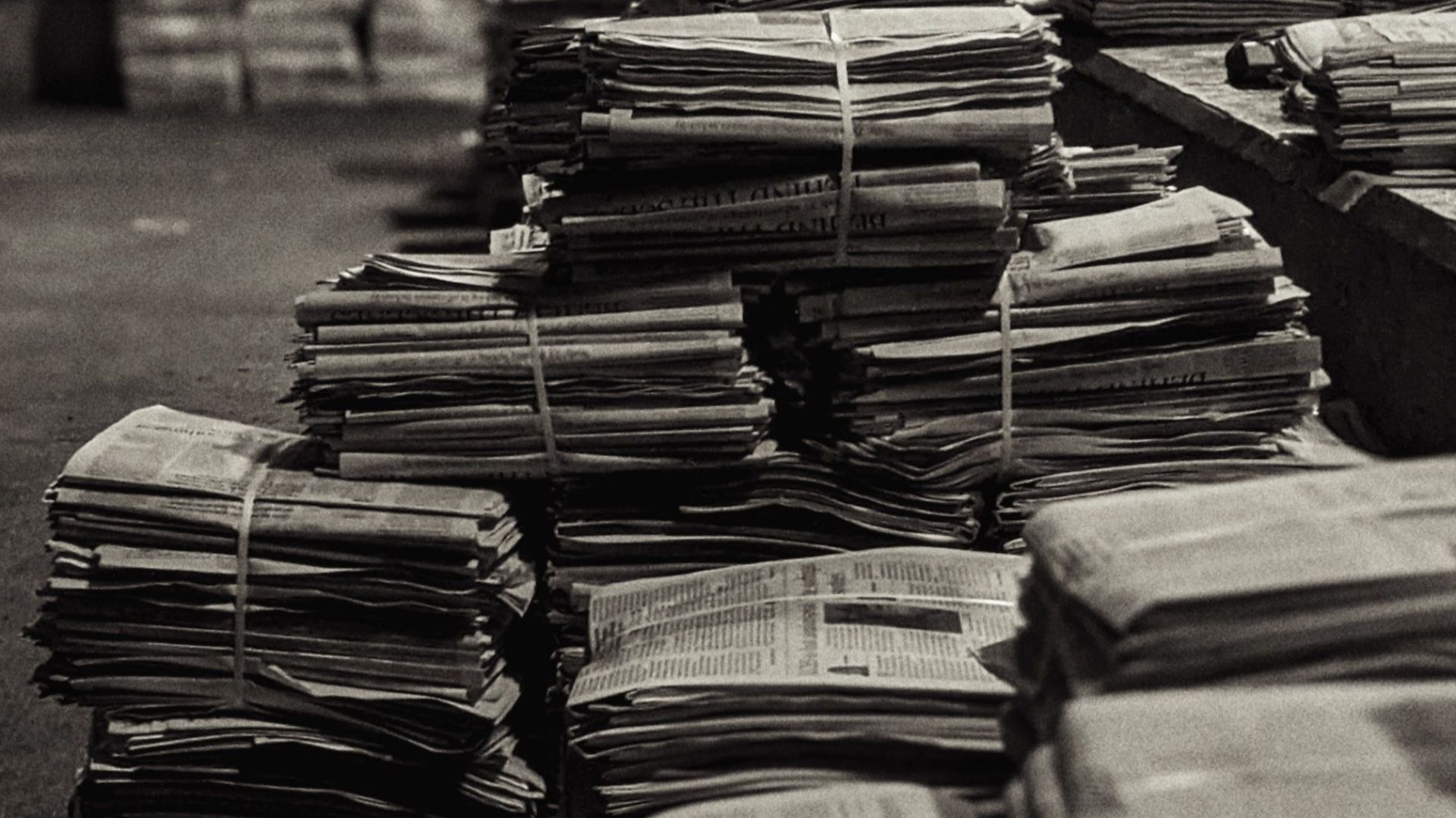 Stacks of newspapers in a warehouse, captured in black and white, creating a vintage feel.