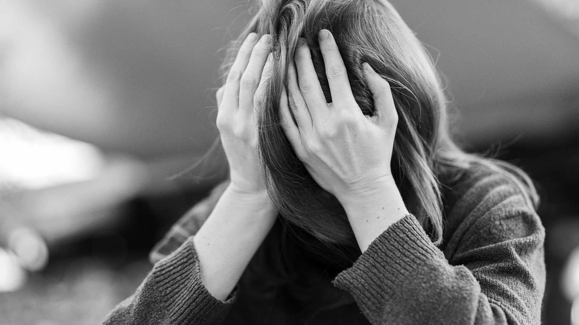 A woman in distress holding her head in her hands, captured in a dramatic black and white portrait.