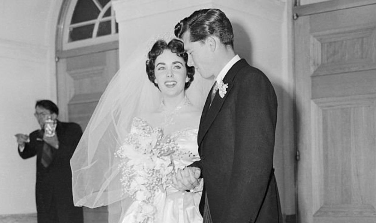 (Original Caption) Mr. and Mrs. Conrad Nicholson Hilton, Jr., stand on the steps of the Church of the Good Shepherd after their wedding. The Bride is Elizabeth Taylor of the movies and the groom is a member of the famous Hilton Hotel family. After a lavish reception, the couple left for a secret honeymoon spot