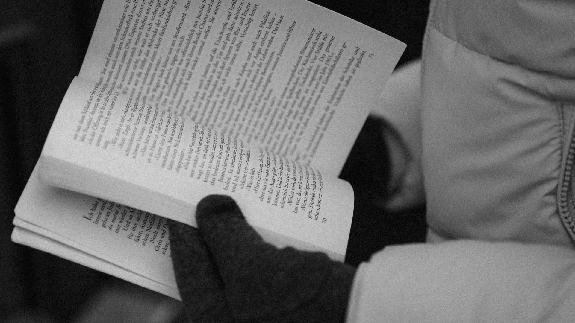Close-up of gloved hands reading a book in black and white, emphasizing literature and cozy winter vibes.