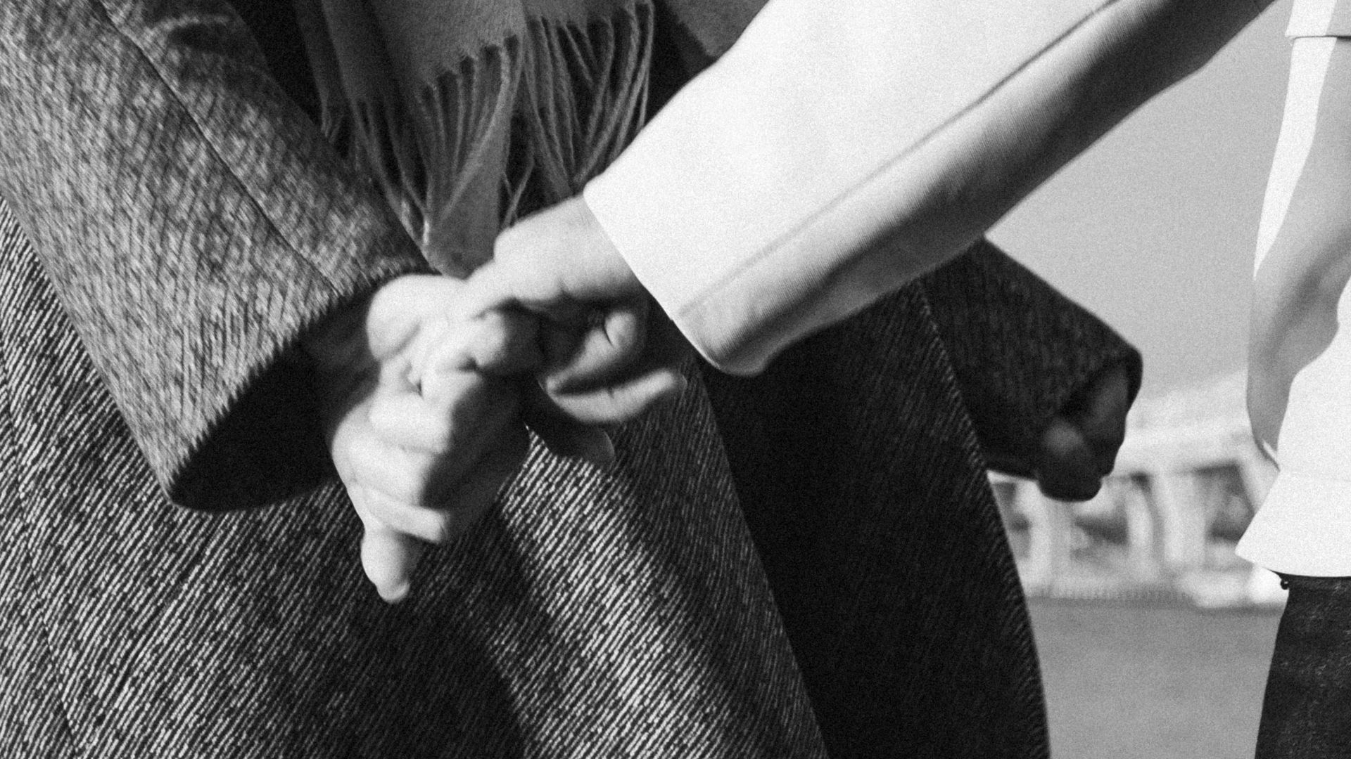 Intimate close-up of a couple holding hands by the water in a black and white photograph.