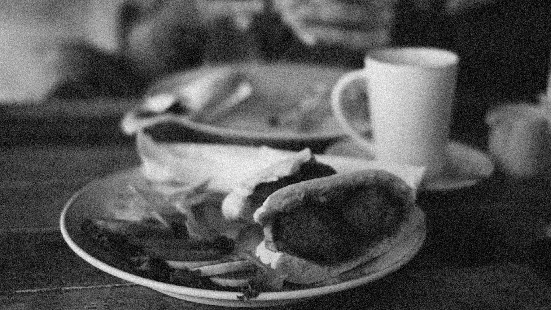 Black and white close-up of a meal with cup on a wooden table.