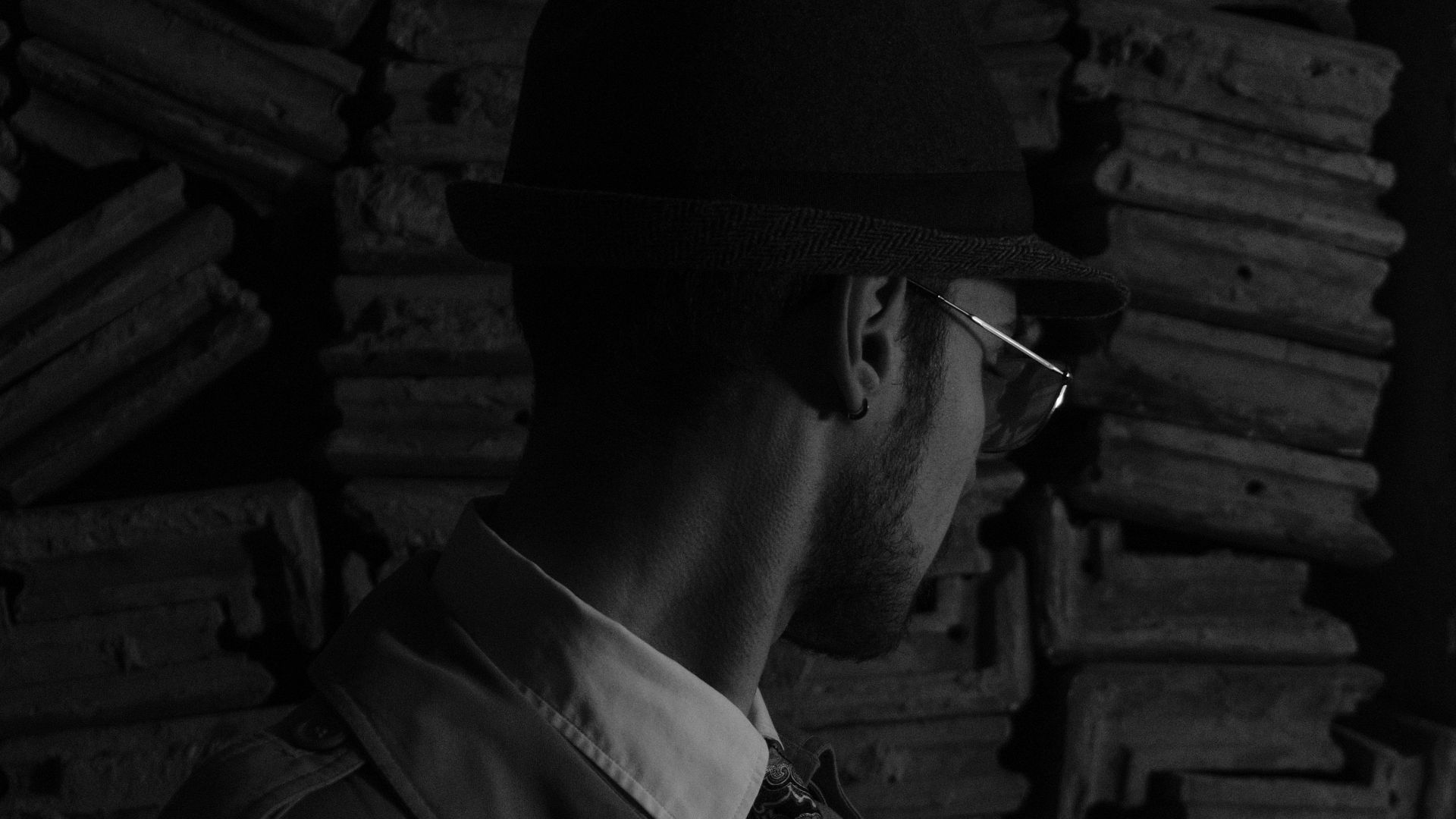 A man in a trench coat and hat touches tiles, evoking a retro, mysterious mood.