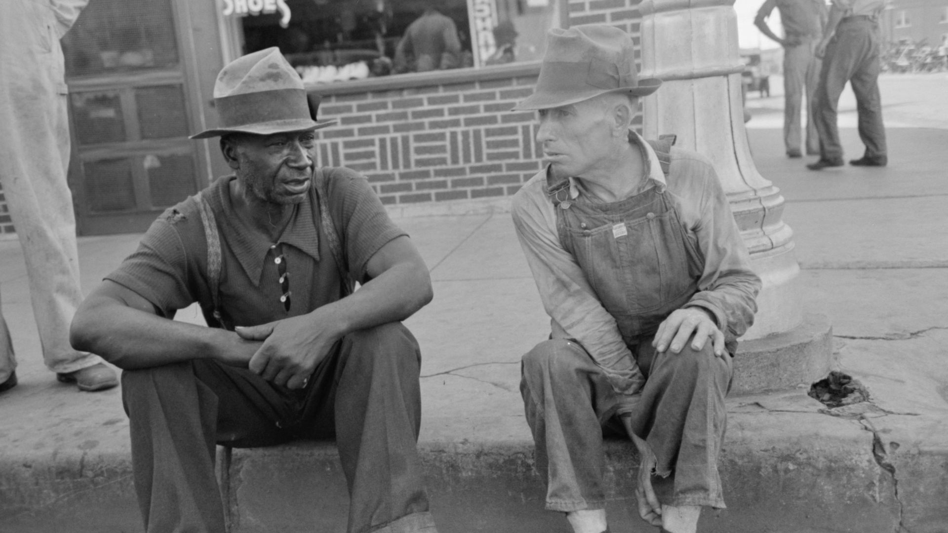 Black and white man sitting on curb talking