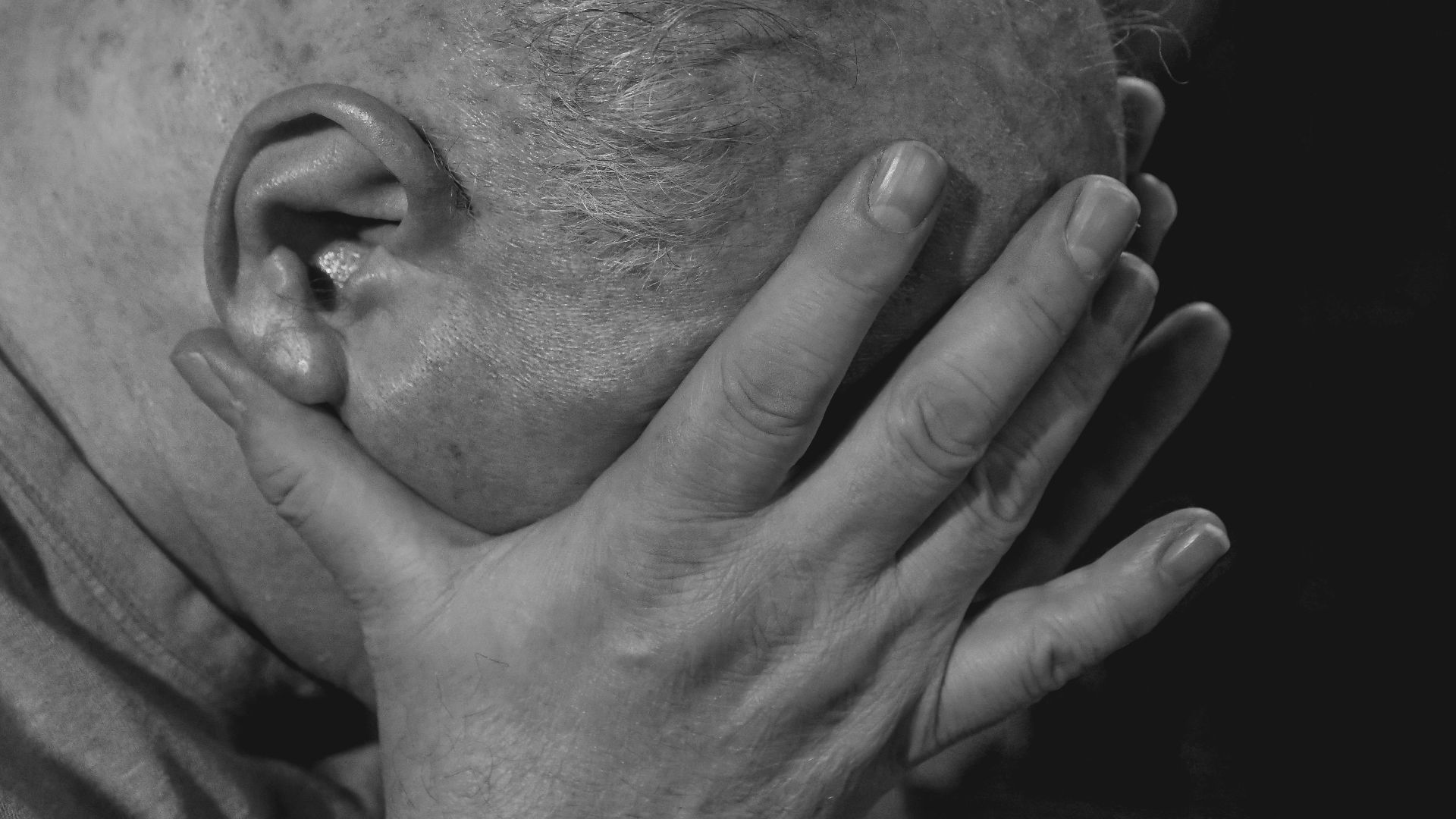 A close-up of an elderly man in black and white showing deep emotion and sadness.