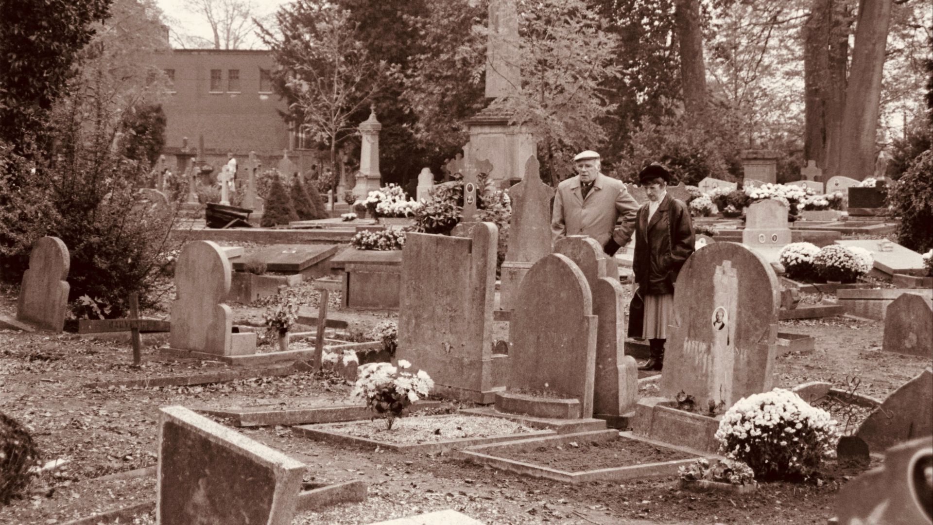 Vintage sepia image of a couple standing in an old cemetery with tombstones.