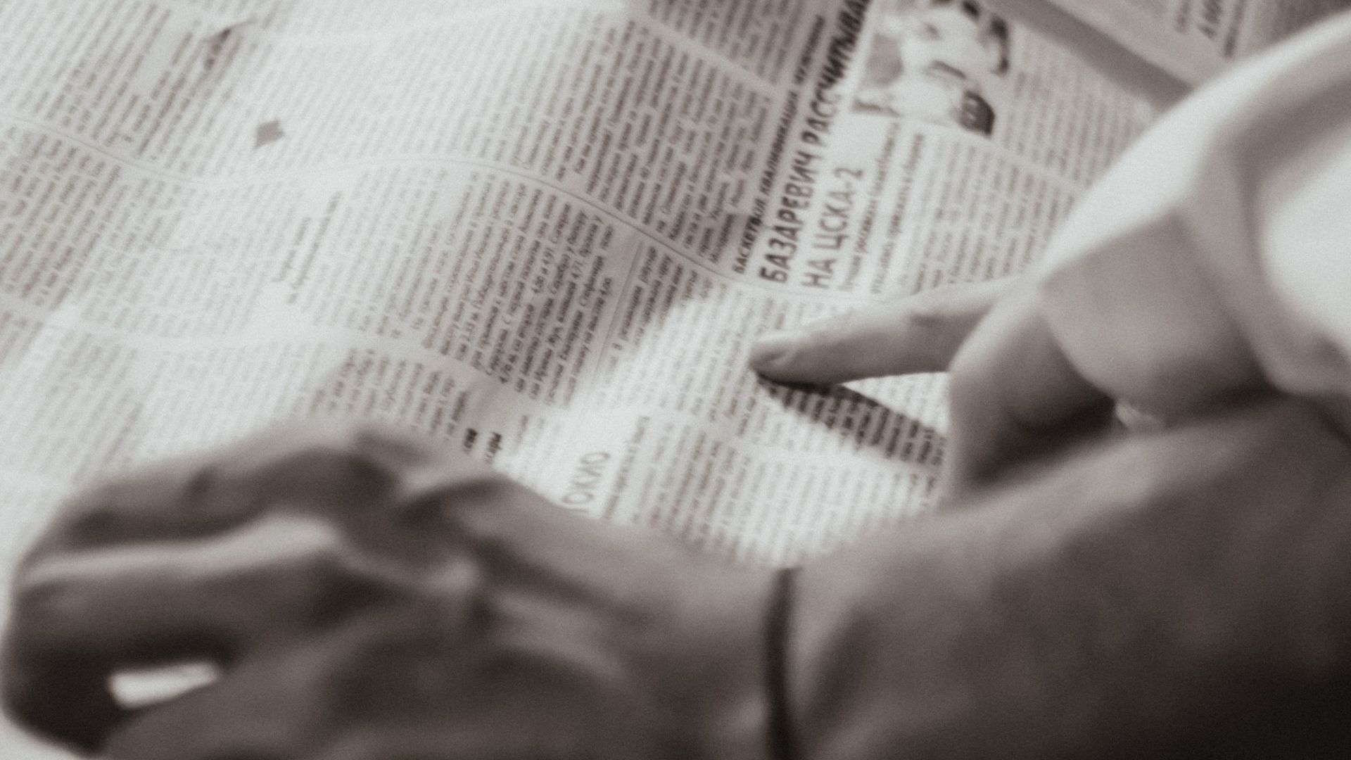 Close-up of hands pointing at a newspaper article with a retro feel in sepia tone.