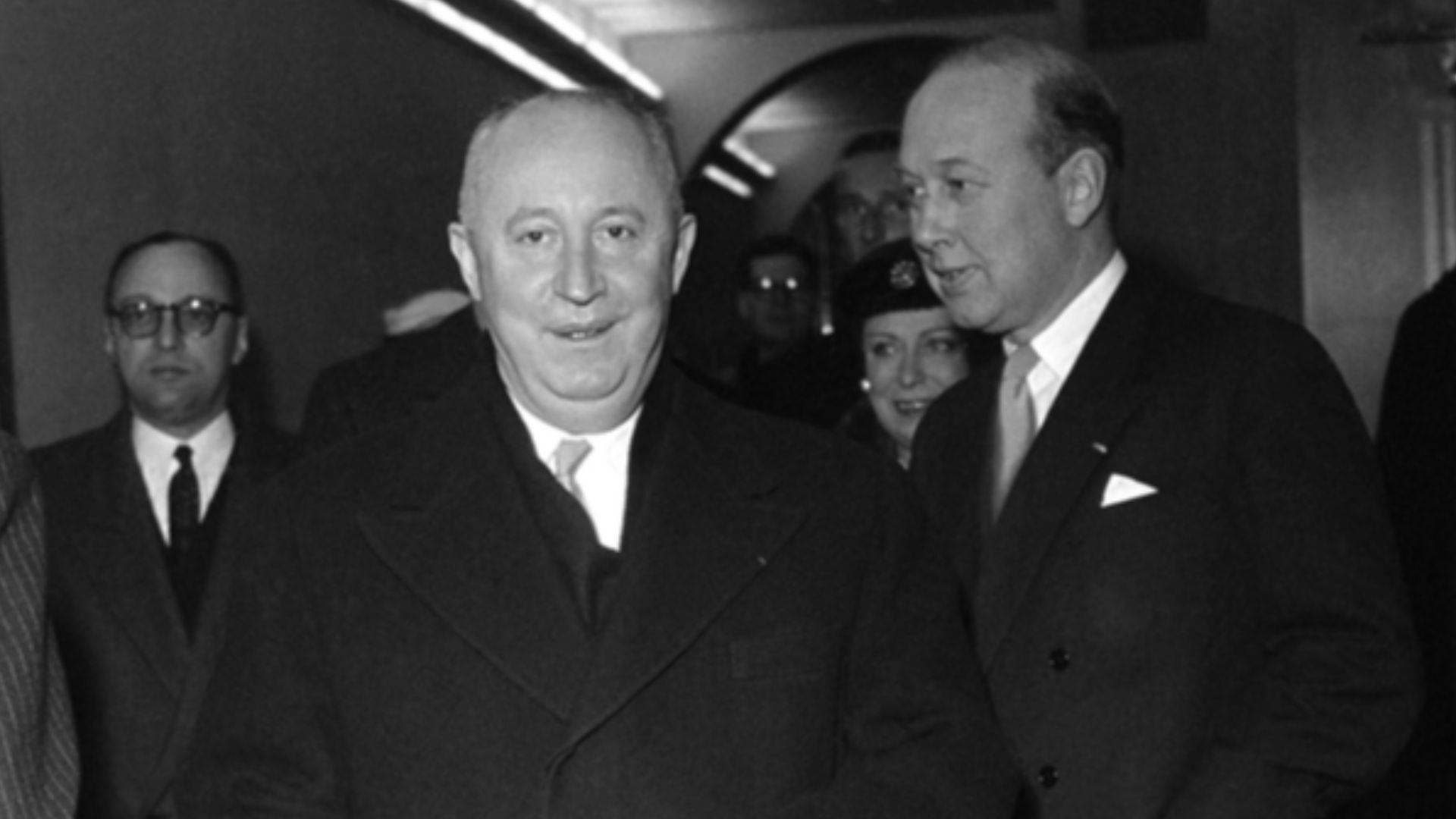 Christian Diors besök på NK, Nordiska kompaniet i Stockholm februari 1957. Personer, bland andra Kurt Jacobsson, står i korridor. Fotografering - februari, 1957 (Känd händelse)