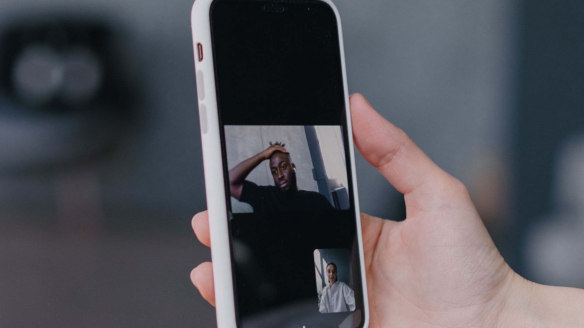 Close-up of a hand holding a smartphone displaying a video call with a blurred background.